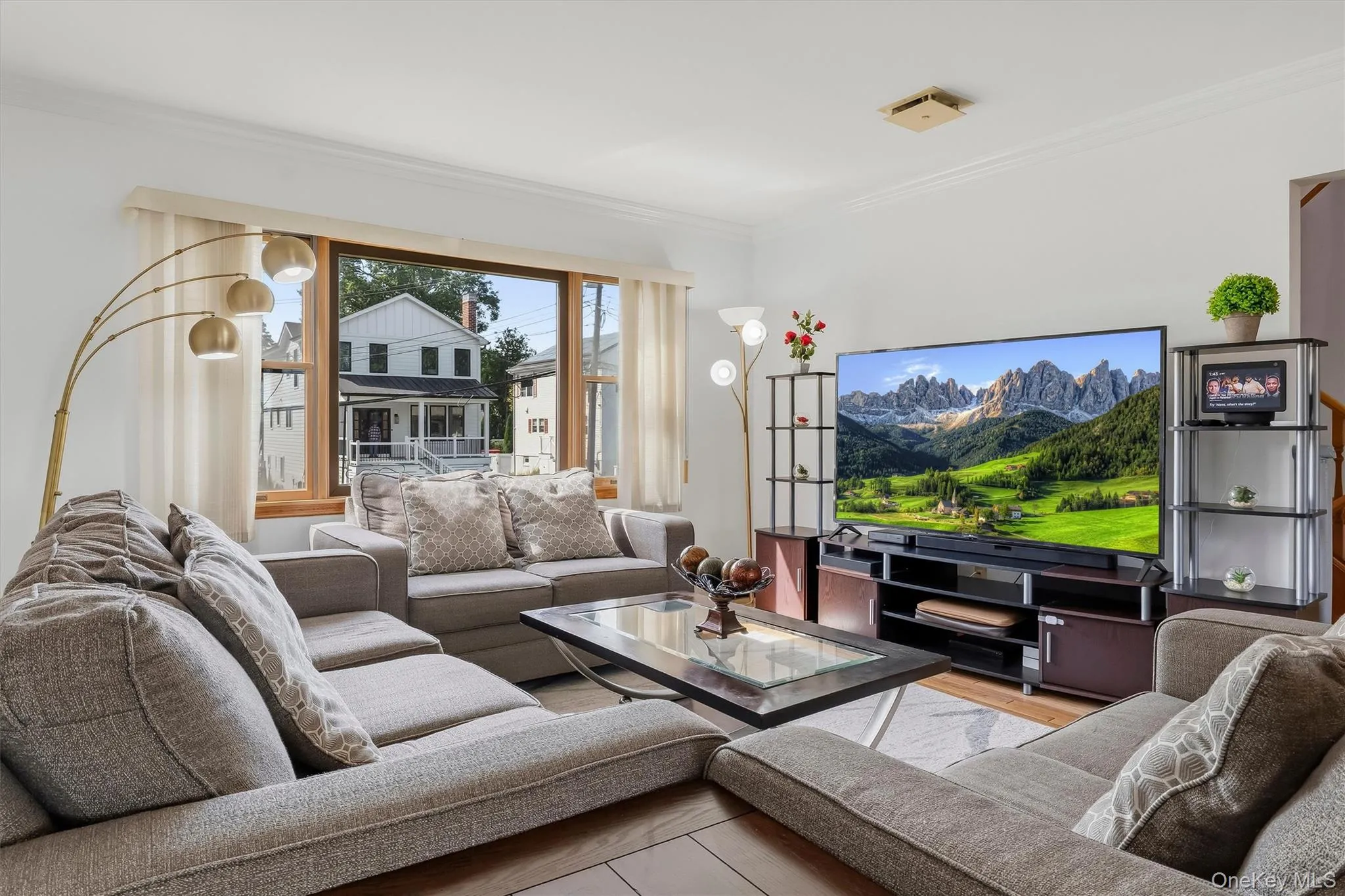Spacious living area featuring large picture windows, wood-finish flooring, and crown molding Spacious living area featuring large picture windows, wood-finish flooring, and crown molding