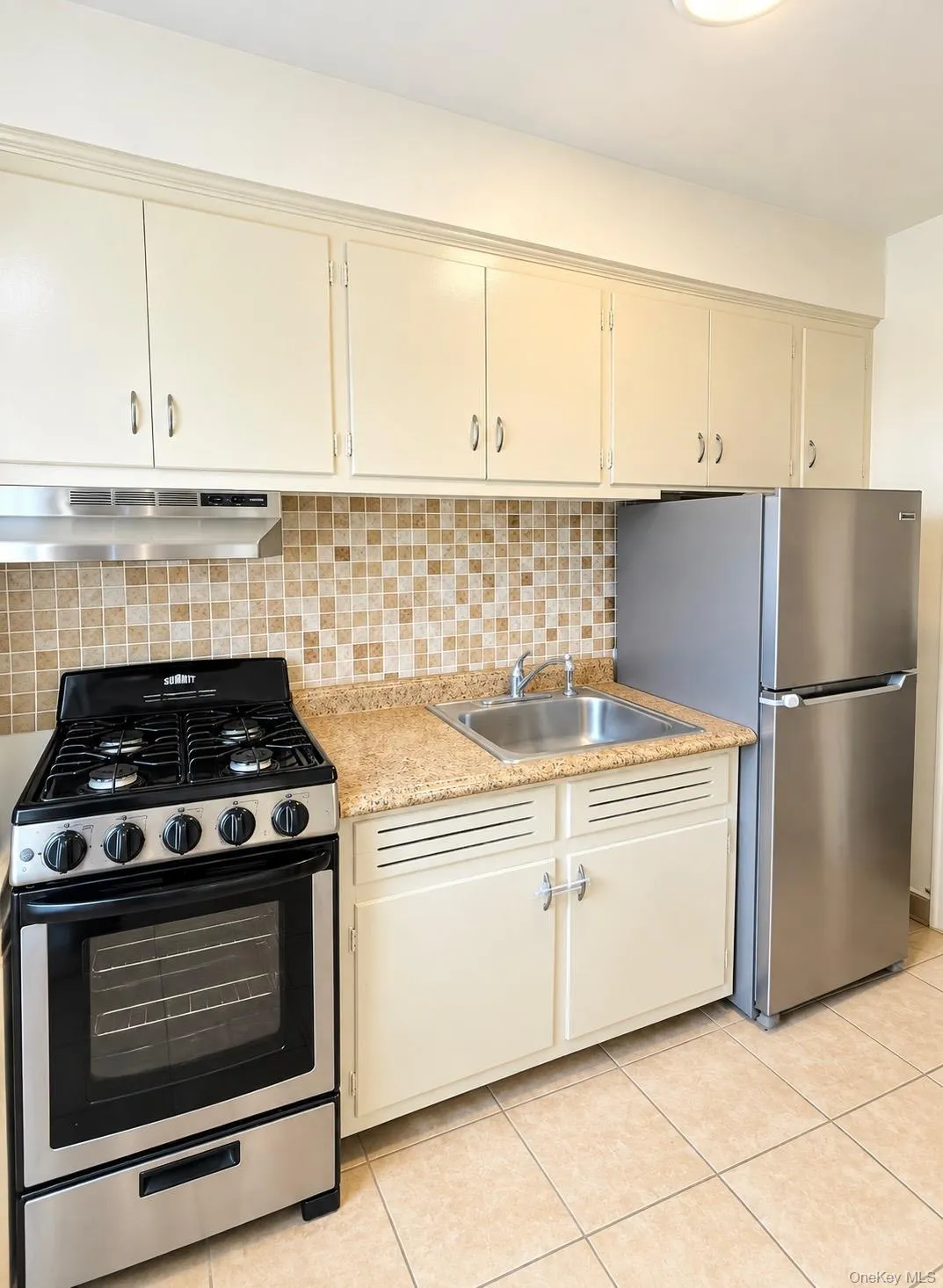 Kitchen featuring stainless steel appliances, light-toned cabinetry, a mosaic tile backsplash, a stainless steel sink, and tile flooring Kitchen featuring stainless steel appliances, light-toned cabinetry, a mosaic tile backsplash, a stainless steel sink, and tile flooring