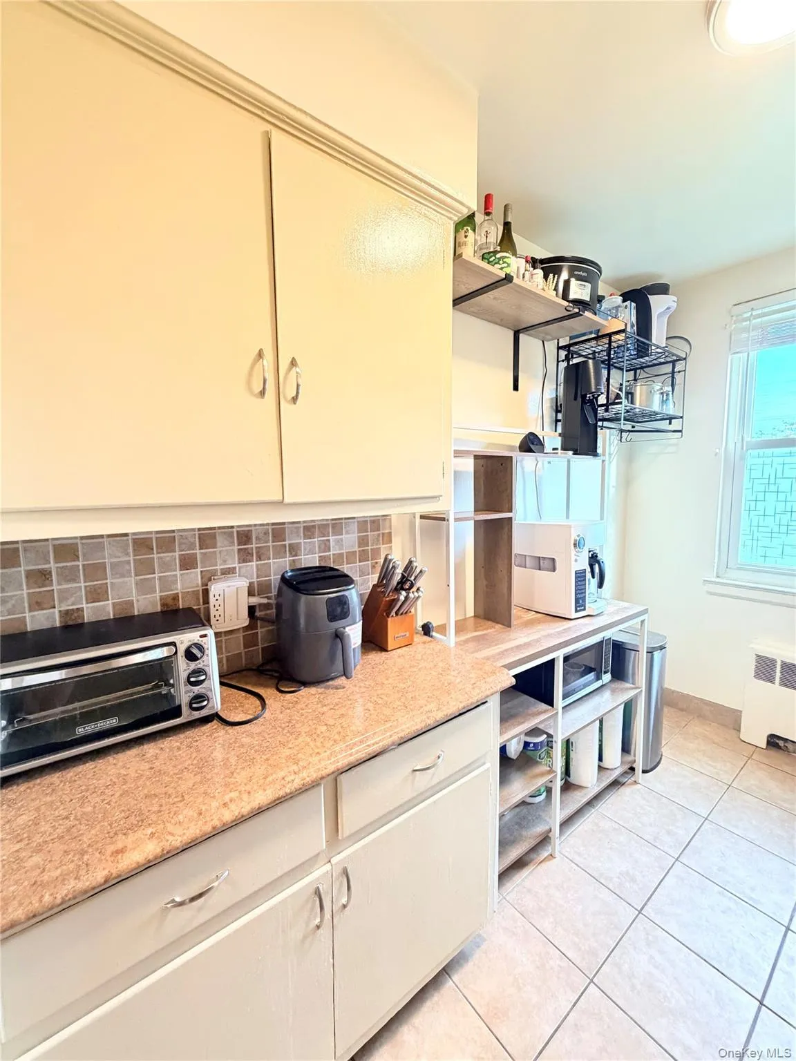 Kitchen featuring light-toned cabinetry, a mosaic tile backsplash, textured countertops, and tiled flooring Kitchen featuring light-toned cabinetry, a mosaic tile backsplash, textured countertops, and tiled flooring