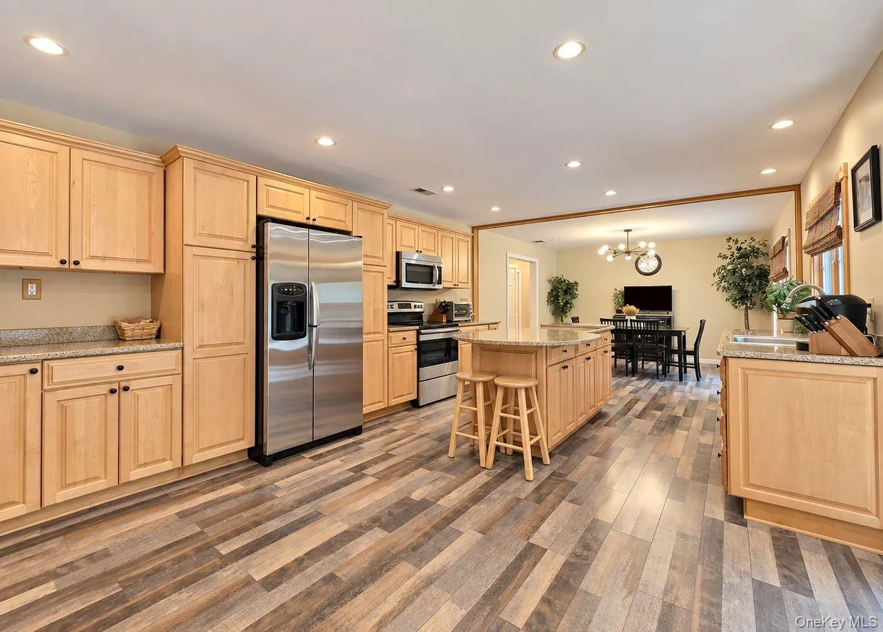Spacious kitchen featuring wood-finish flooring, light wood cabinetry, stainless steel appliances, and an island with a stone countertop Spacious kitchen featuring wood-finish flooring, light wood cabinetry, stainless steel appliances, and an island with a stone countertop