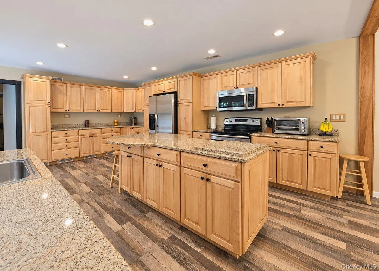 Spacious kitchen featuring extensive light wood cabinetry, stone countertops, a large center island, wood-finish flooring, and recessed lighting Spacious kitchen featuring extensive light wood cabinetry, stone countertops, a large center island, wood-finish flooring, and recessed lighting