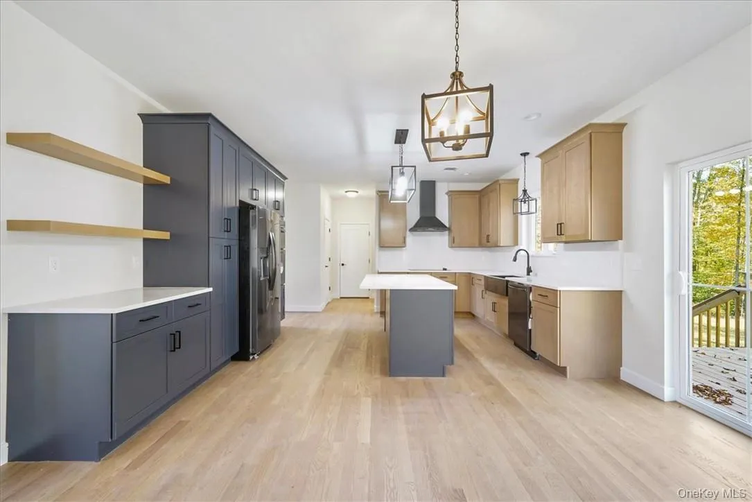 Kitchen with a center island, stainless steel appliances, light hardwood / wood-style floors, wall chimney range hood, and decorative light fixtures Kitchen with a center island, stainless steel appliances, light hardwood / wood-style floors, wall chimney range hood, and decorative light fixtures
