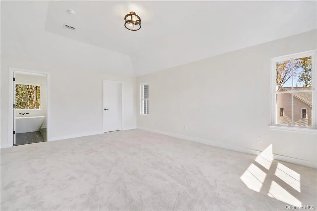Unfurnished bedroom featuring light carpet, vaulted ceiling, and multiple windows Unfurnished bedroom featuring light carpet, vaulted ceiling, and multiple windows