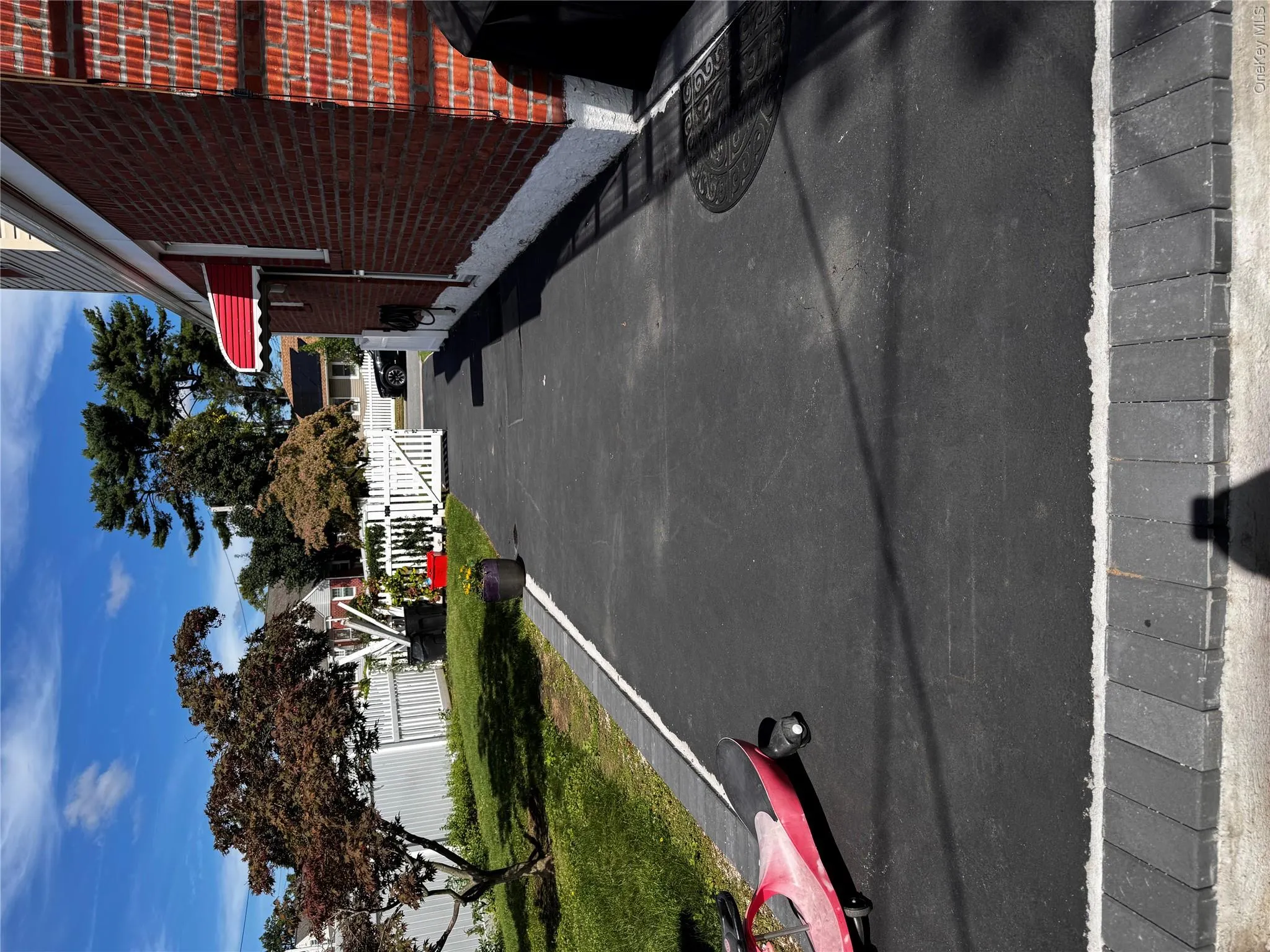 Brick exterior with a red fabric awning, asphalt driveway, and a white picket fence Brick exterior with a red fabric awning, asphalt driveway, and a white picket fence