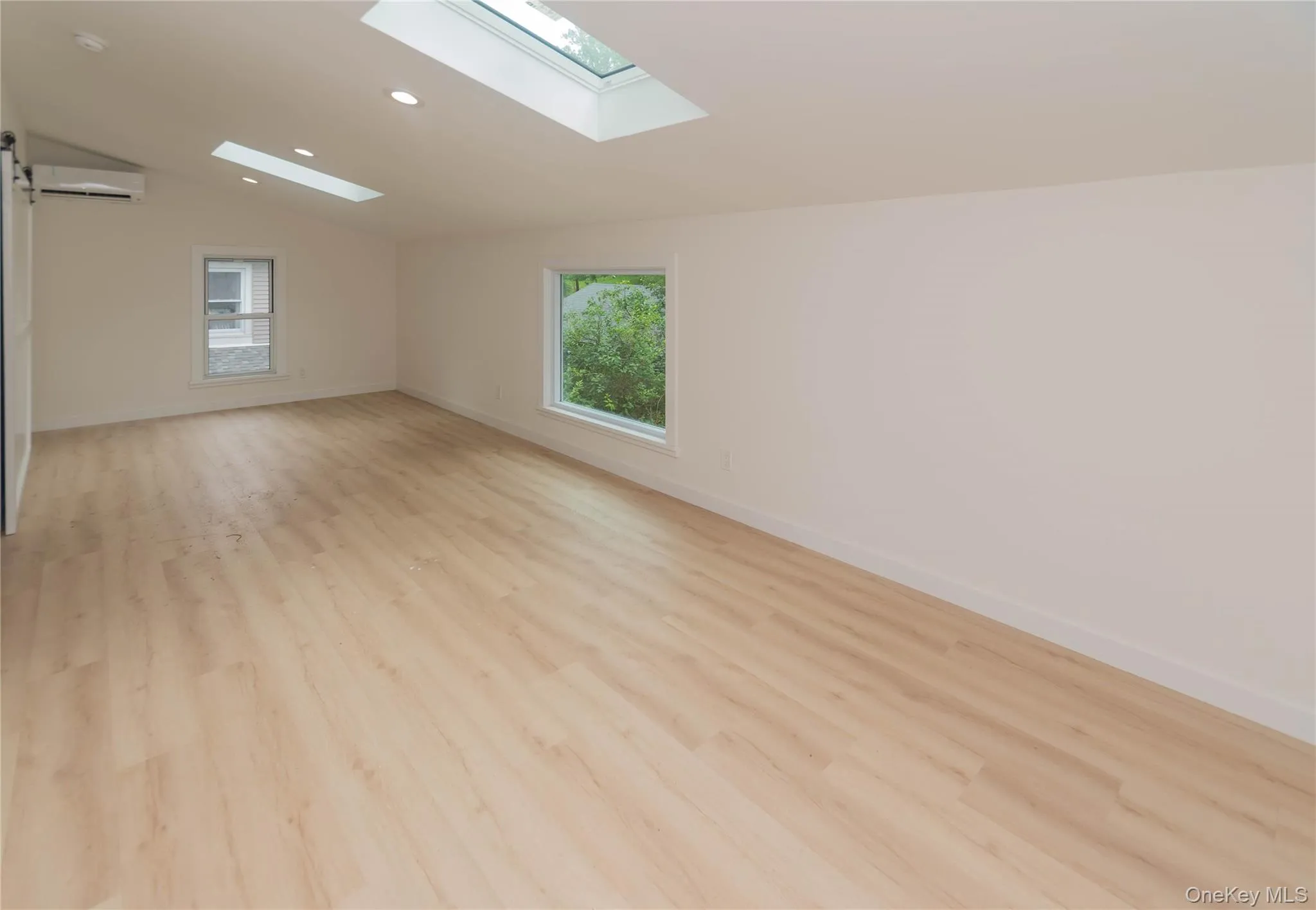 Spacious room featuring wood-finish flooring, two skylights, recessed lighting, and a ductless mini-split system Spacious room featuring wood-finish flooring, two skylights, recessed lighting, and a ductless mini-split system