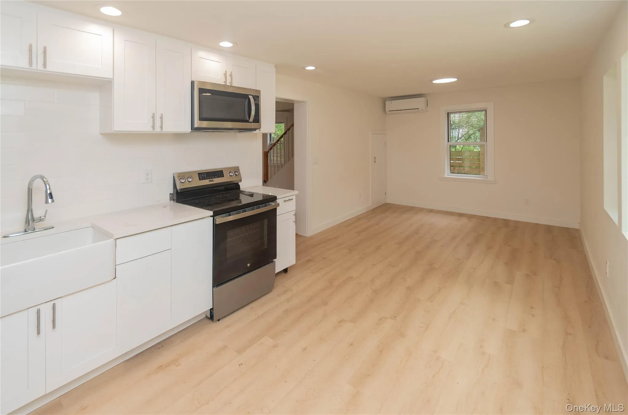 White cabinetry, stainless steel appliances, farmhouse sink, light wood-finish flooring, and recessed lighting White cabinetry, stainless steel appliances, farmhouse sink, light wood-finish flooring, and recessed lighting