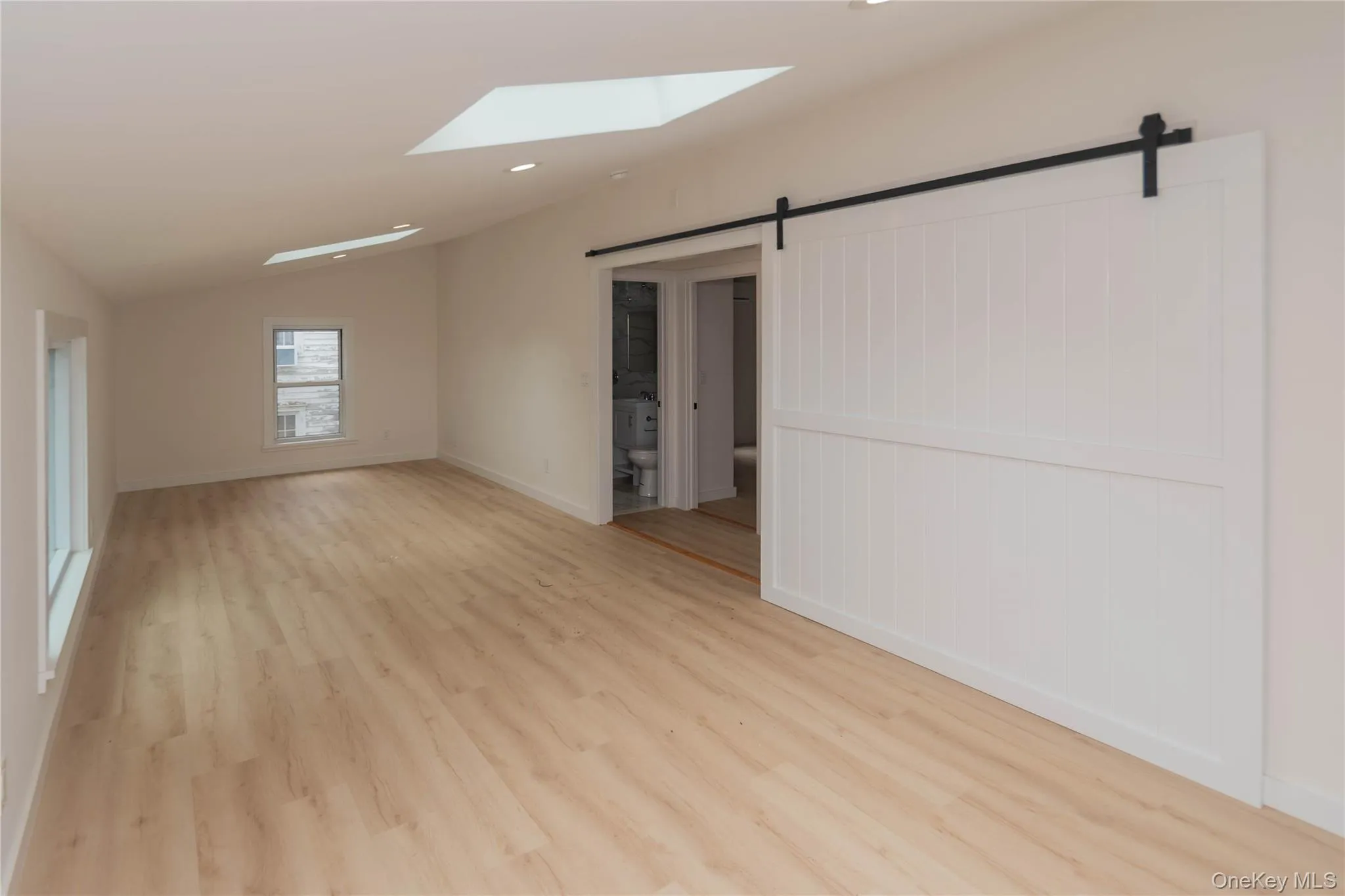 Expansive room featuring skylights, recessed lighting, wood-finish flooring, a contemporary sliding barn door, and multiple windows Expansive room featuring skylights, recessed lighting, wood-finish flooring, a contemporary sliding barn door, and multiple windows