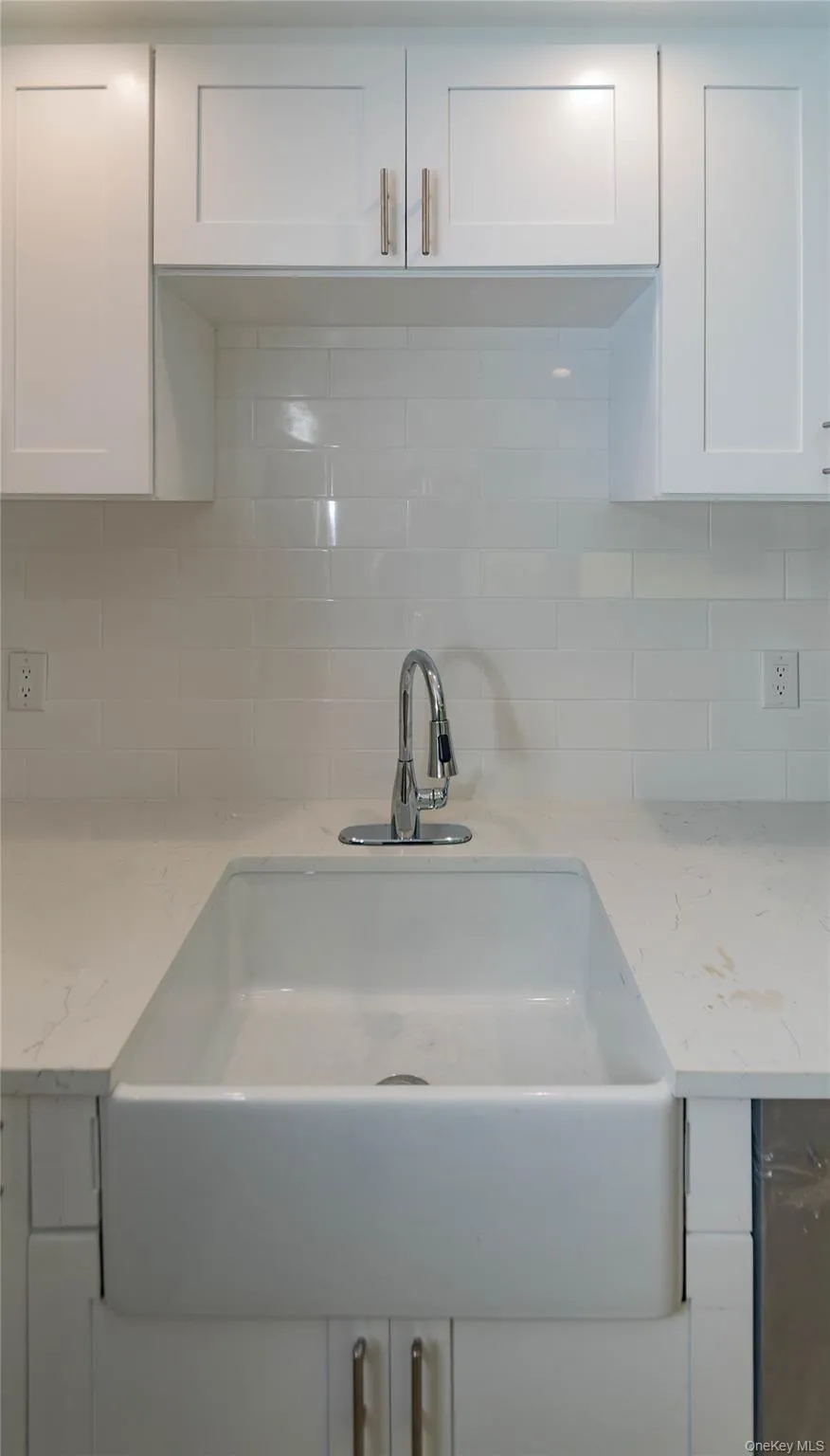 White shaker-style cabinetry, undermount apron-front sink, polished chrome faucet, white subway tile backsplash, and light-toned countertops White shaker-style cabinetry, undermount apron-front sink, polished chrome faucet, white subway tile backsplash, and light-toned countertops