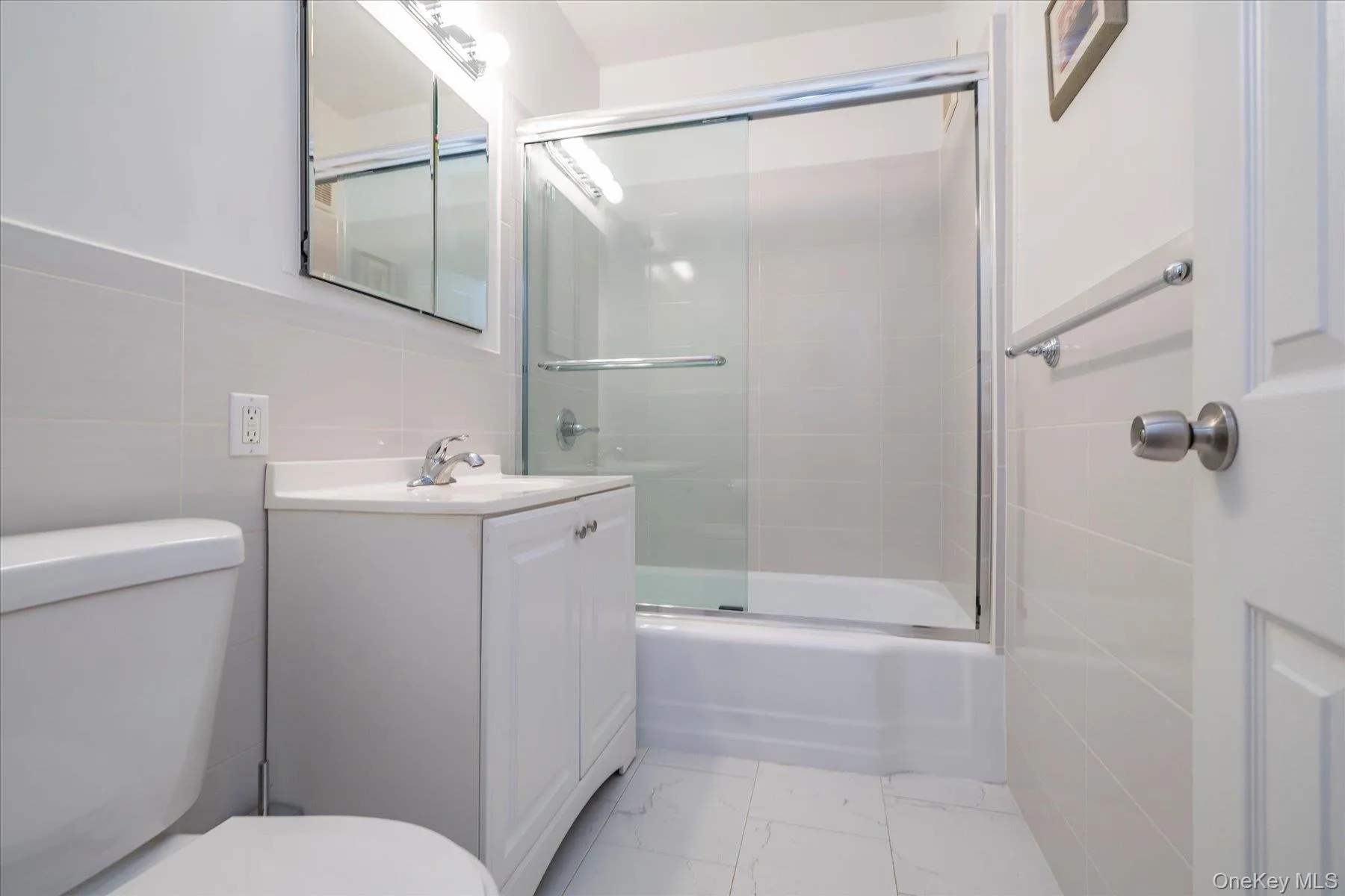 White vanity with integrated sink, glass-enclosed shower/tub combination, and tiled walls White vanity with integrated sink, glass-enclosed shower/tub combination, and tiled walls