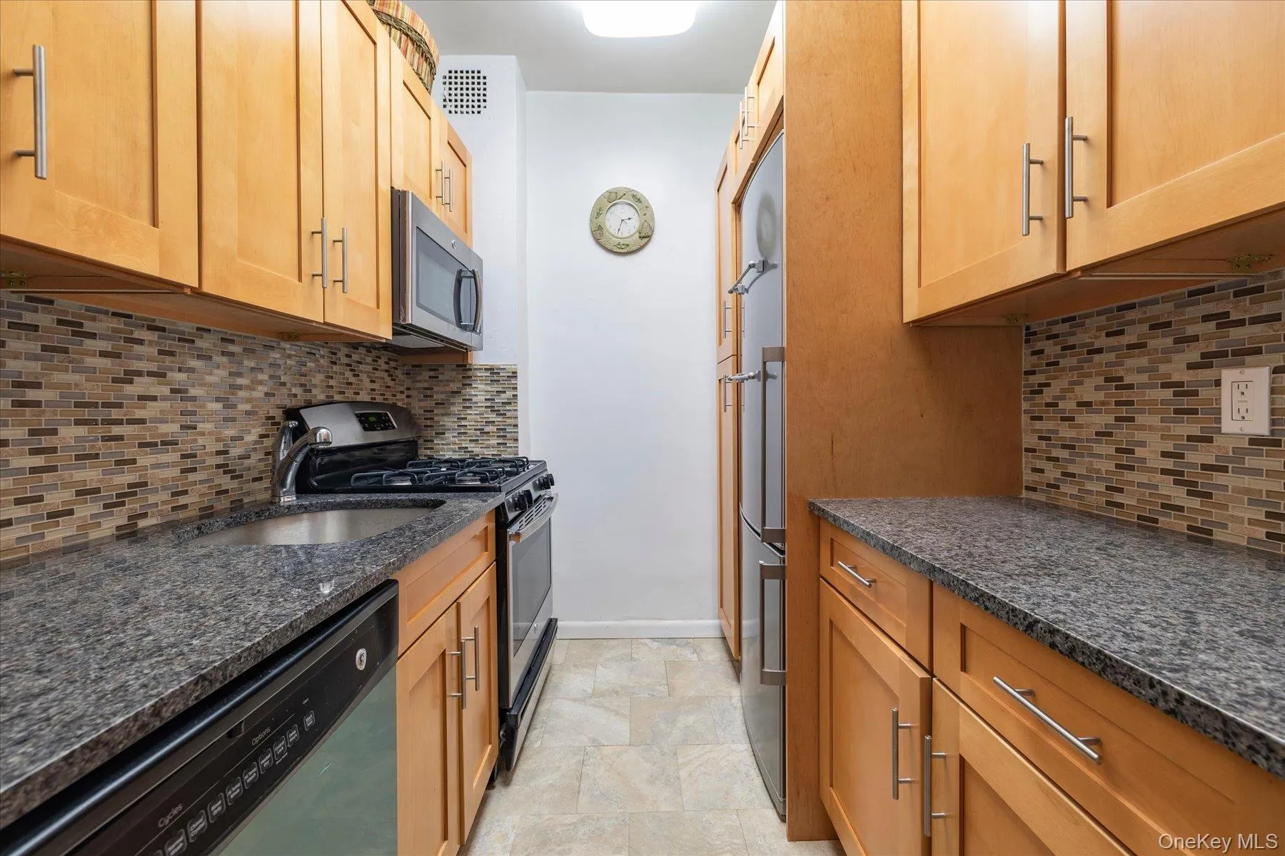 Kitchen featuring wood-finish cabinetry, dark granite-style countertops, stainless steel appliances, and a mosaic tile backsplash Kitchen featuring wood-finish cabinetry, dark granite-style countertops, stainless steel appliances, and a mosaic tile backsplash