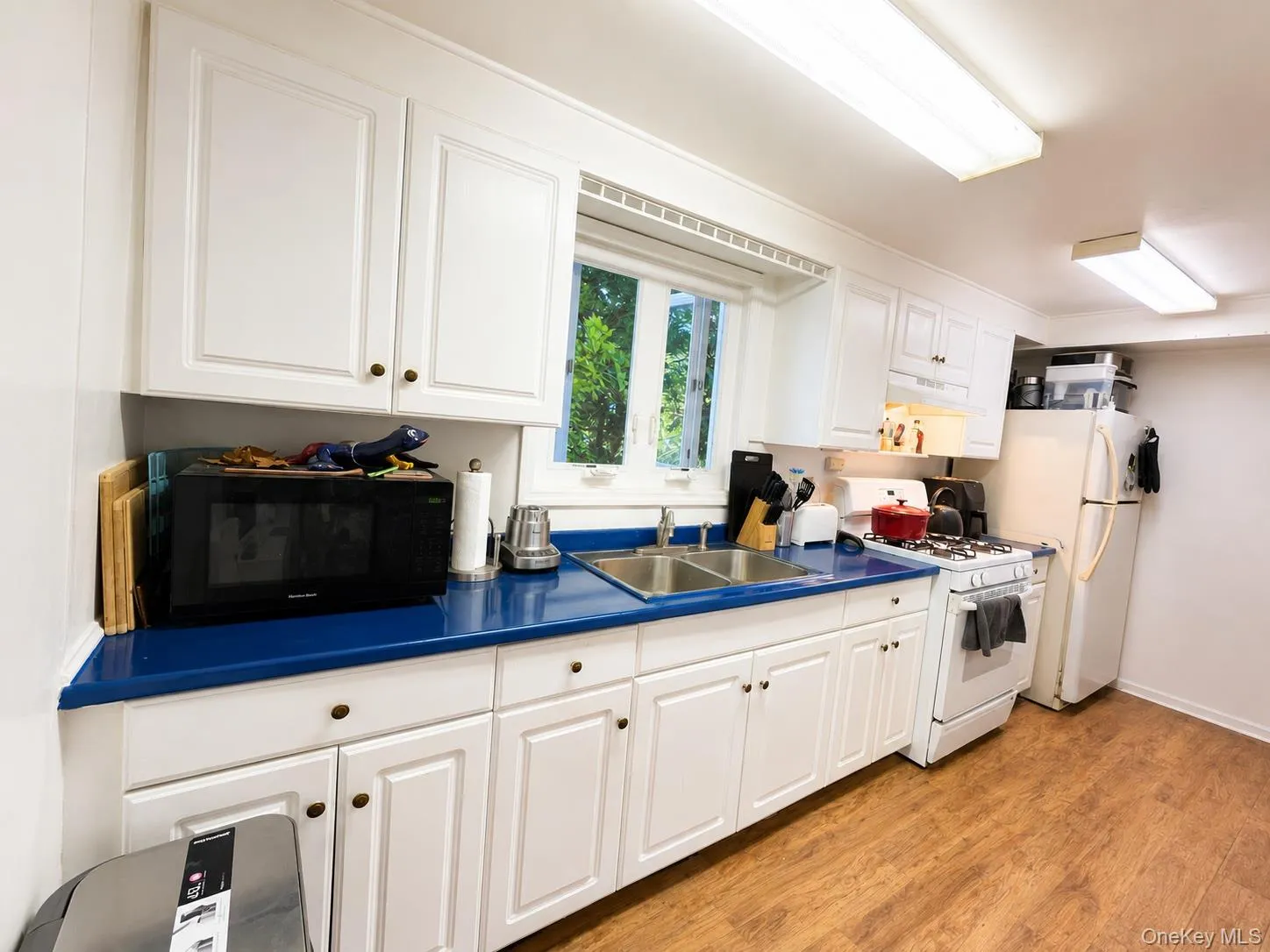 White cabinetry with brass-finish hardware, blue countertops, a double basin sink, and wood-finish flooring White cabinetry with brass-finish hardware, blue countertops, a double basin sink, and wood-finish flooring