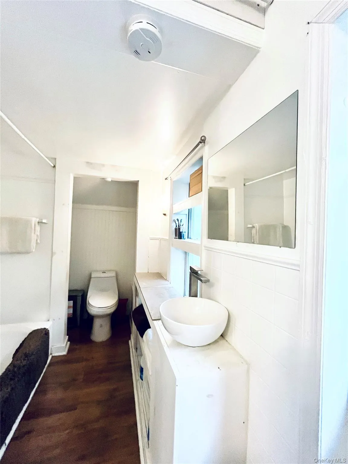 Wood-finish flooring, white vanity with integrated vessel sink, polished chrome faucet, and white subway tile surround Wood-finish flooring, white vanity with integrated vessel sink, polished chrome faucet, and white subway tile surround