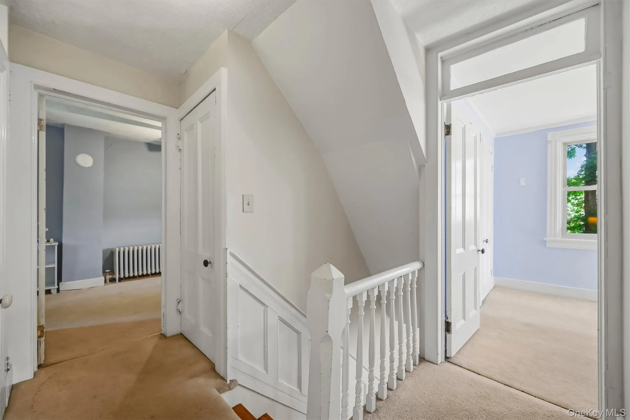 Carpeted hallway with white painted balusters and railings, featuring two paneled doors and a window with white trim Carpeted hallway with white painted balusters and railings, featuring two paneled doors and a window with white trim