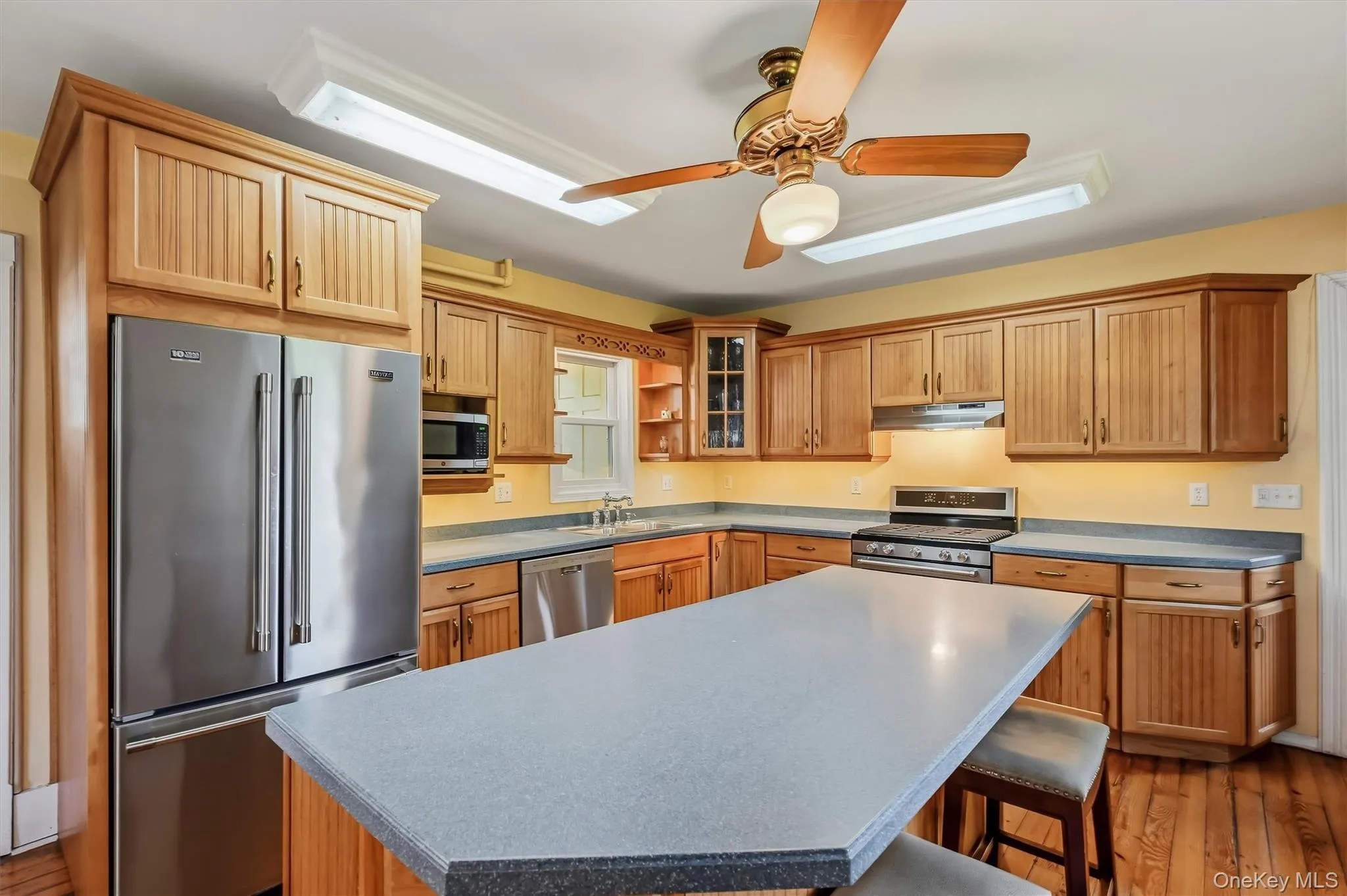 Kitchen featuring wood cabinetry, stainless steel appliances, a center island with countertop seating, and wood-finish flooring Kitchen featuring wood cabinetry, stainless steel appliances, a center island with countertop seating, and wood-finish flooring