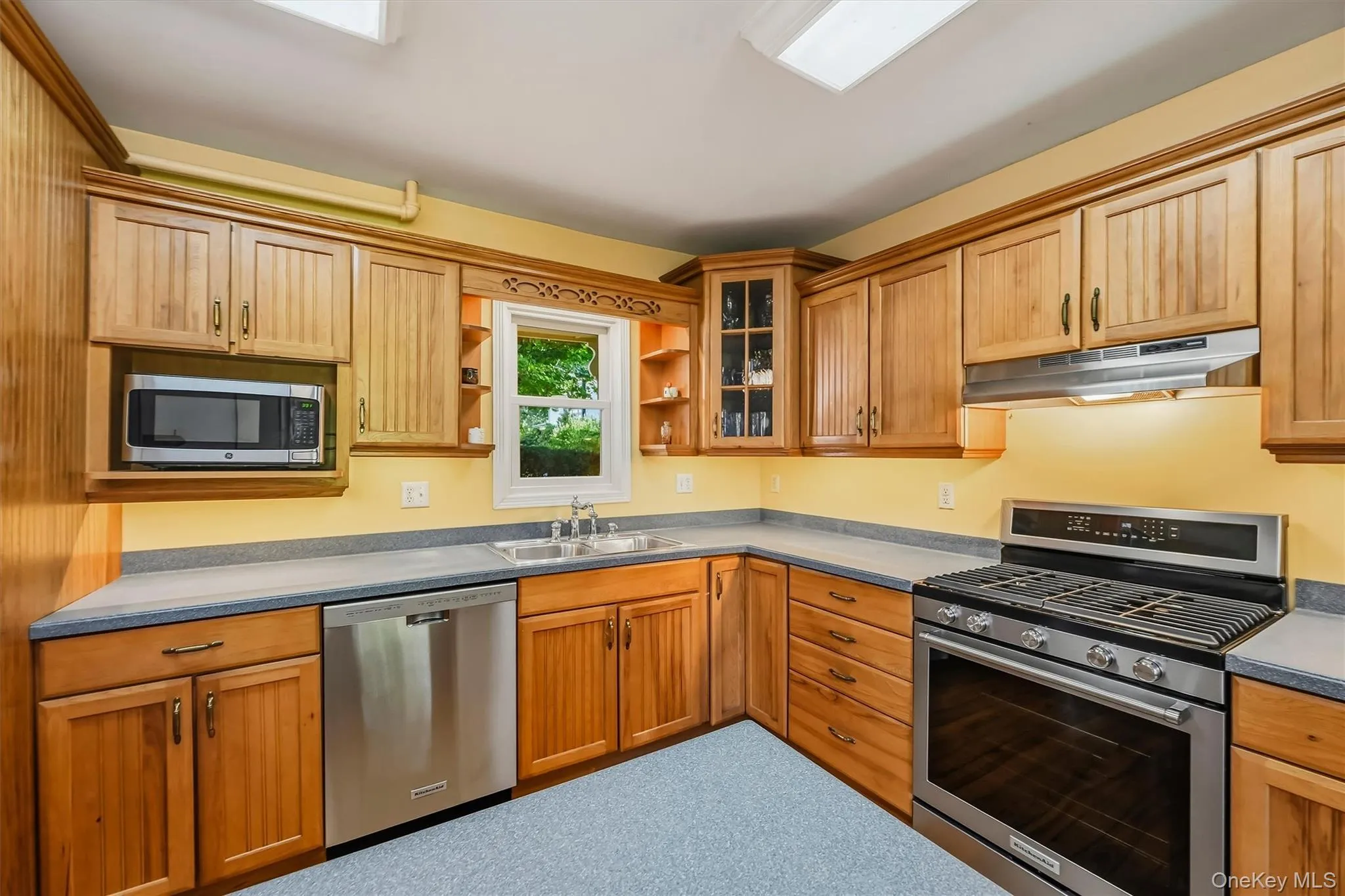 Wood-finish cabinetry with display cabinet, stainless steel appliances, and a built-in microwave Wood-finish cabinetry with display cabinet, stainless steel appliances, and a built-in microwave