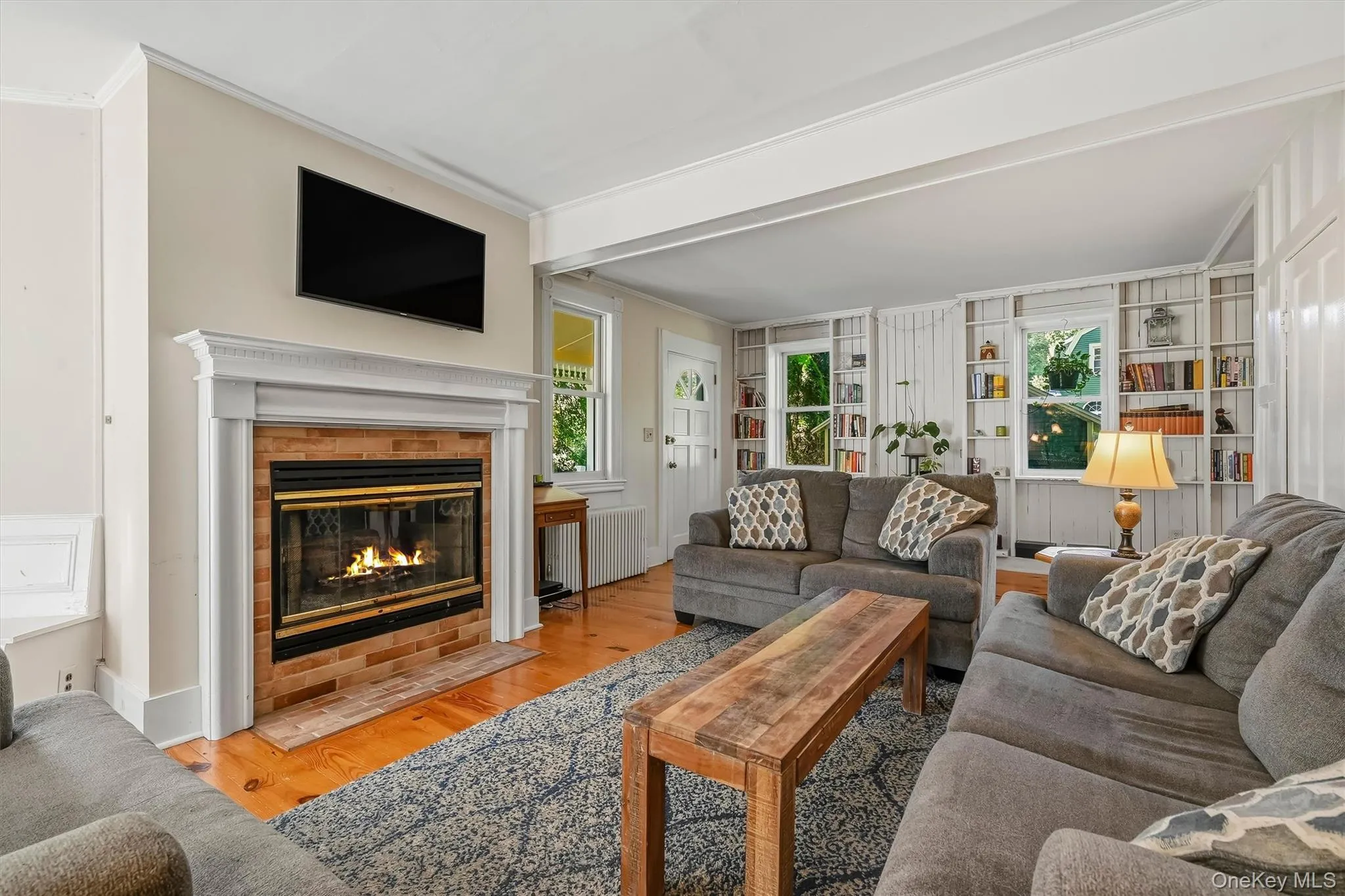 Fireplace with a white mantle and brick surround, hardwood flooring, built-in shelving, and white trim work Fireplace with a white mantle and brick surround, hardwood flooring, built-in shelving, and white trim work