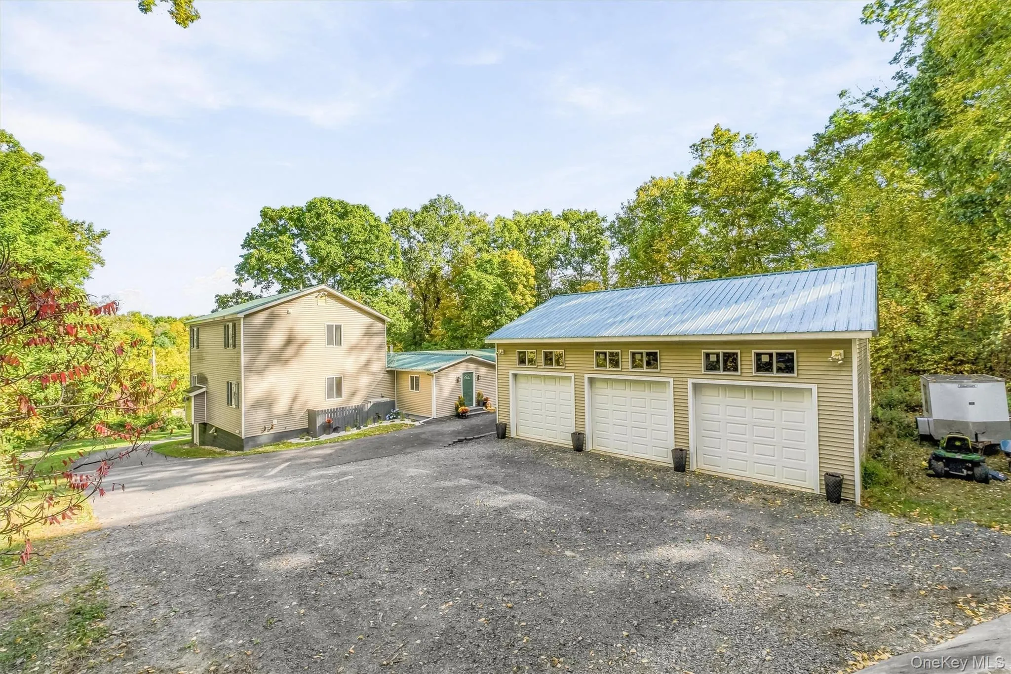 Three-bay detached garage with a metal roof and transom windows, accompanied by a two-story residence featuring a green metal roof Three-bay detached garage with a metal roof and transom windows, accompanied by a two-story residence featuring a green metal roof