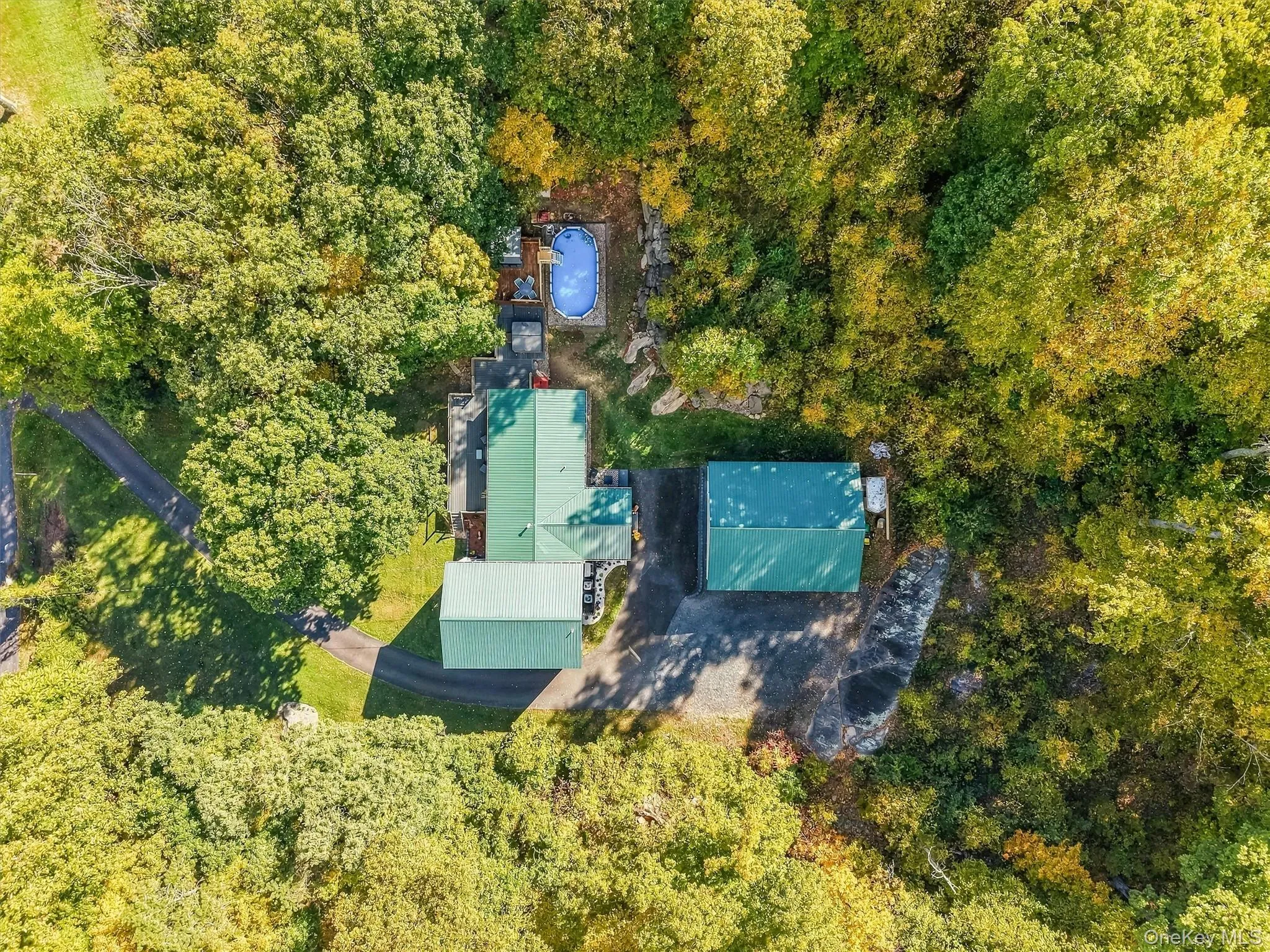 Lush natural surroundings with mature trees, multiple outbuildings, an above-ground pool with surrounding decking, and a paved driveway Lush natural surroundings with mature trees, multiple outbuildings, an above-ground pool with surrounding decking, and a paved driveway