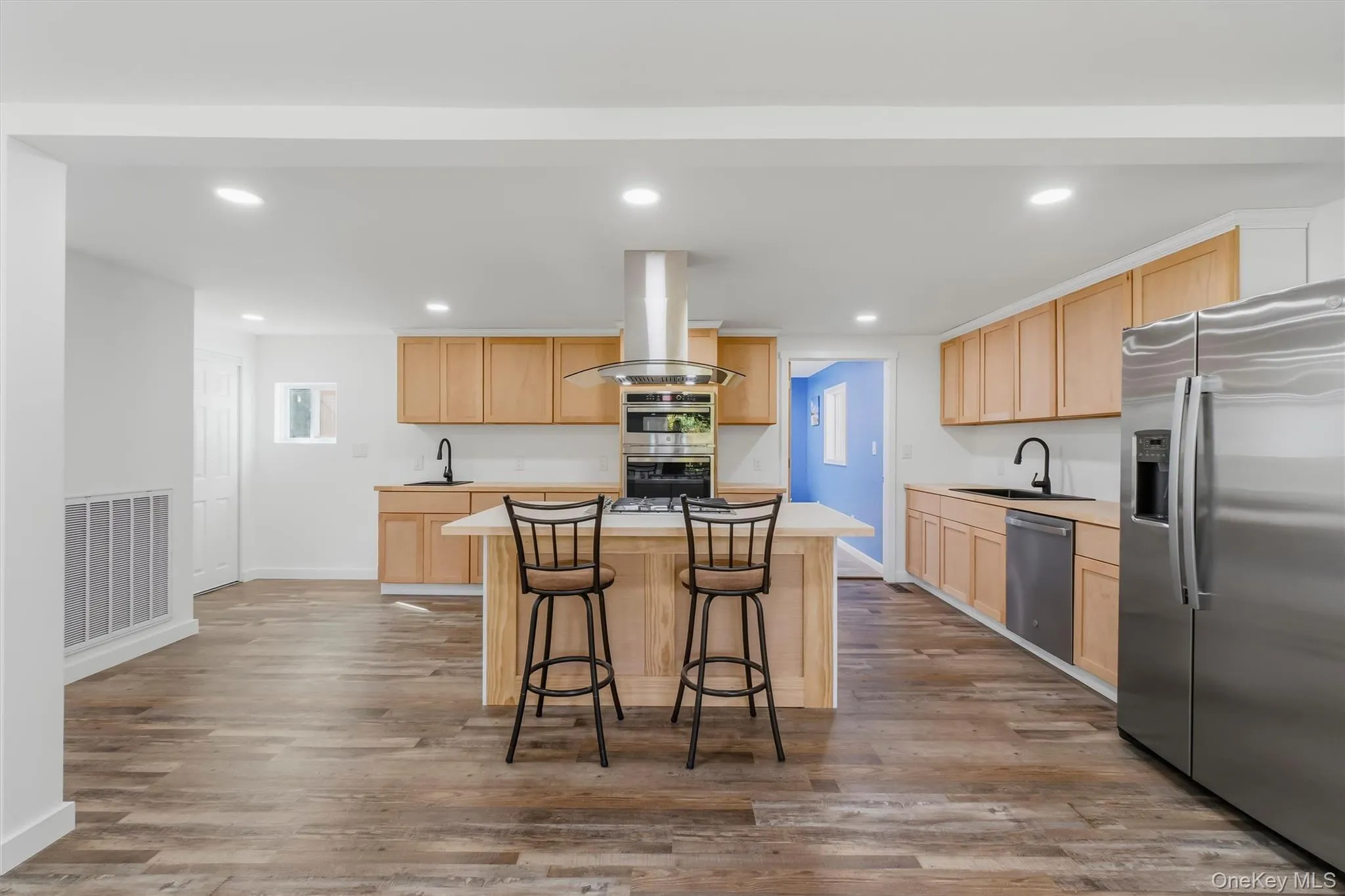 Kitchen featuring wood-finish flooring, recessed lighting, wood cabinetry, a center island, and stainless steel appliances Kitchen featuring wood-finish flooring, recessed lighting, wood cabinetry, a center island, and stainless steel appliances