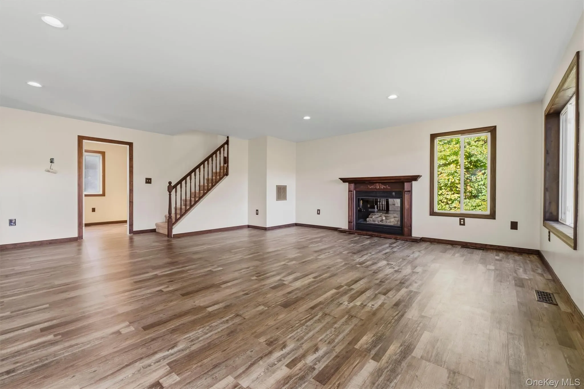 Recessed ceiling lighting, wood-finish flooring, dark wood trim, fireplace with dark wood mantel, and a staircase with wood railing Recessed ceiling lighting, wood-finish flooring, dark wood trim, fireplace with dark wood mantel, and a staircase with wood railing