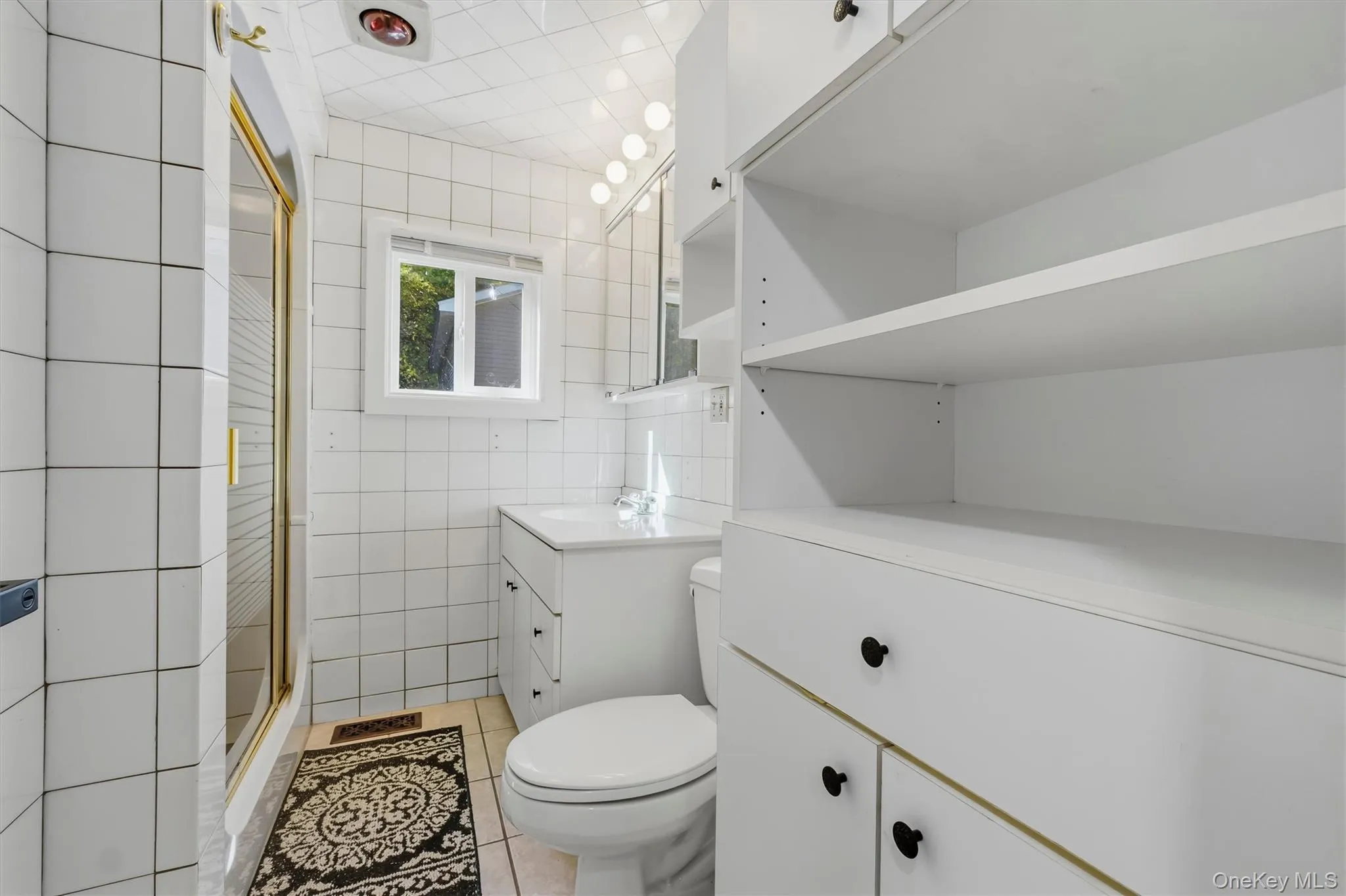 White tiled bathroom featuring a shower with a gold-toned frame, a vanity with an integrated sink, a built-in toilet, and extensive white cabinetry White tiled bathroom featuring a shower with a gold-toned frame, a vanity with an integrated sink, a built-in toilet, and extensive white cabinetry