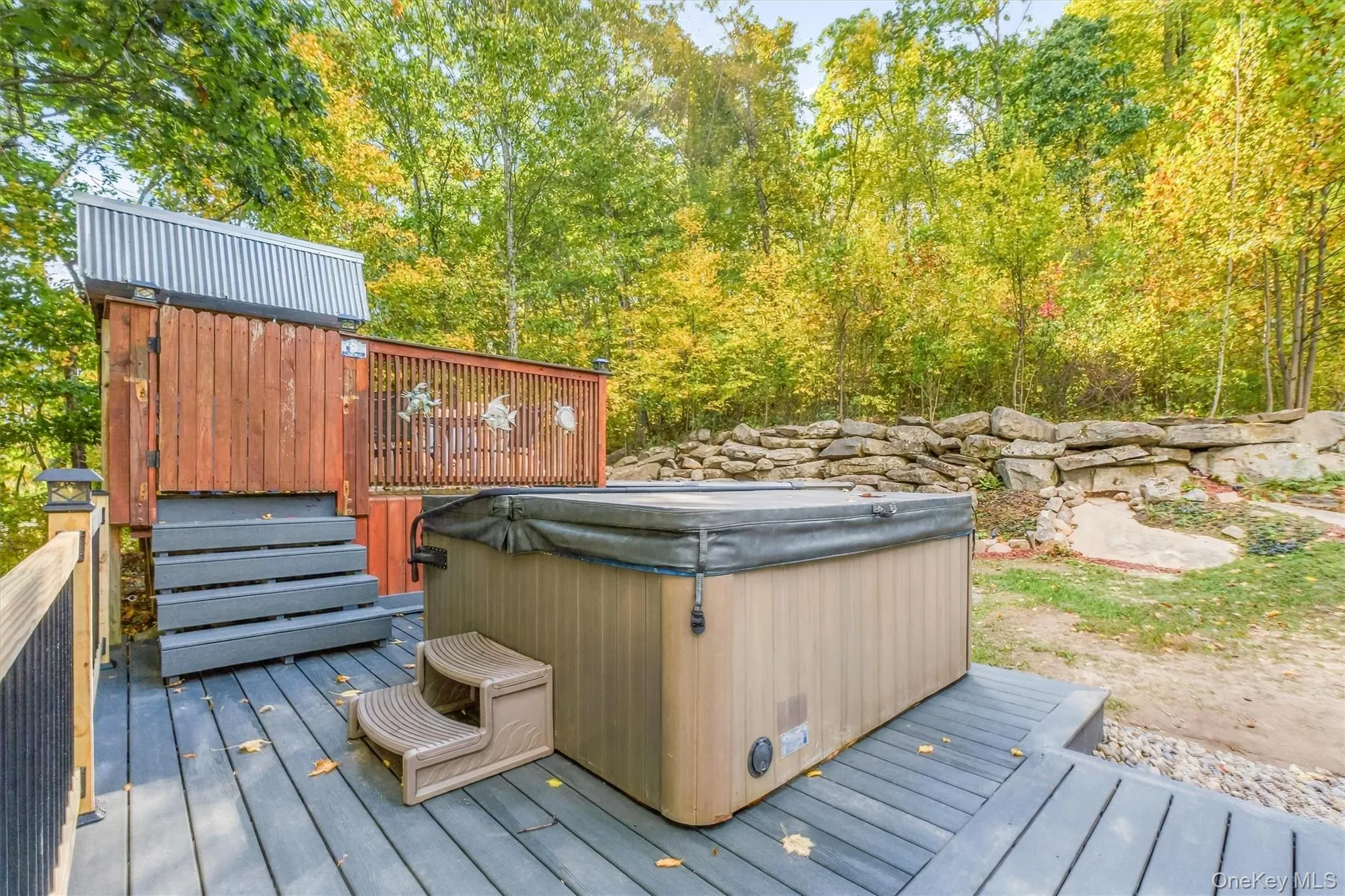 Expansive outdoor deck featuring a hot tub, a privacy screen, and a surrounding natural rock landscaping Expansive outdoor deck featuring a hot tub, a privacy screen, and a surrounding natural rock landscaping