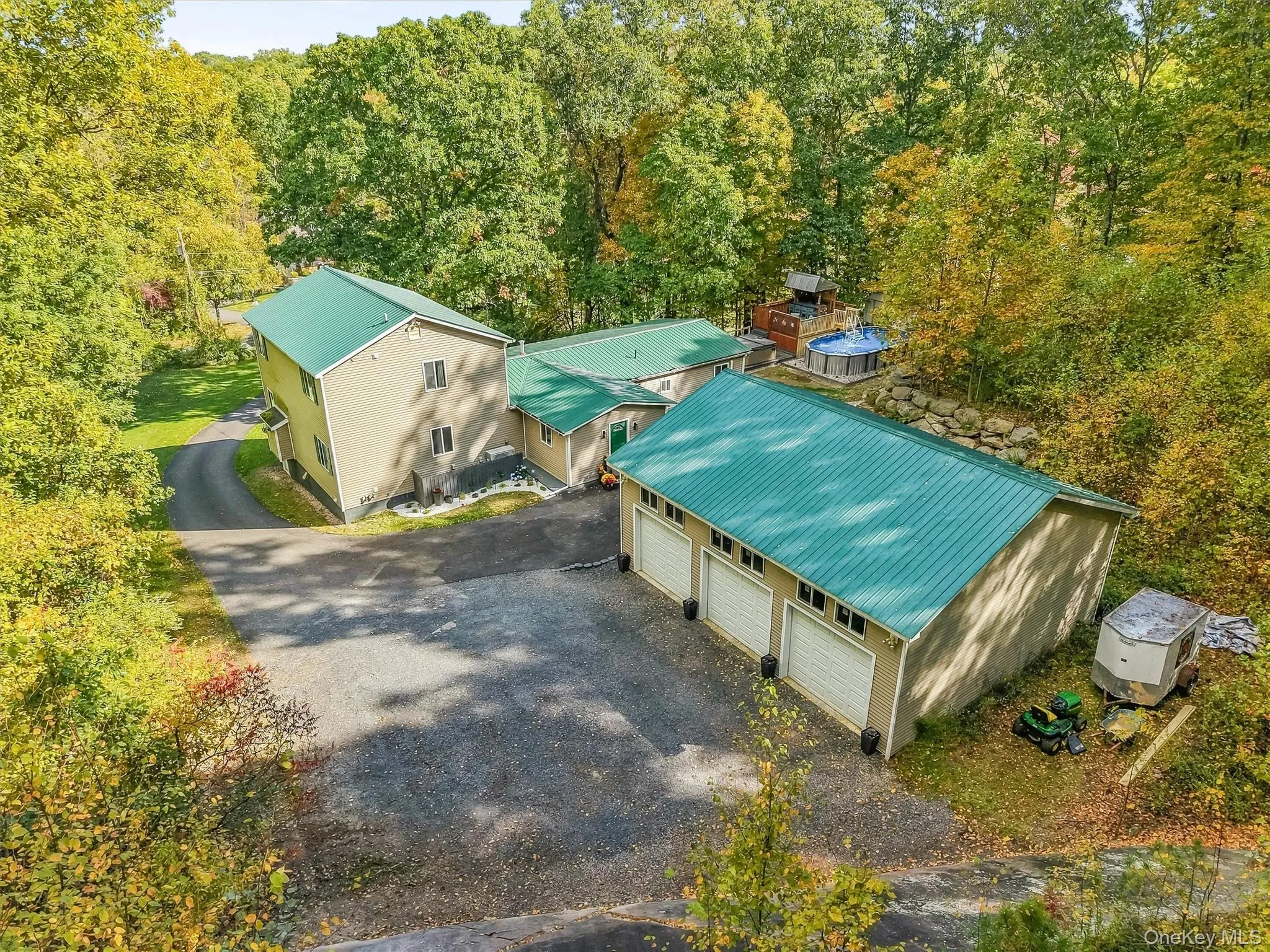 Multiple structures with green metal roofing, extensive paved driveway, and a multi-car garage with three bays Multiple structures with green metal roofing, extensive paved driveway, and a multi-car garage with three bays