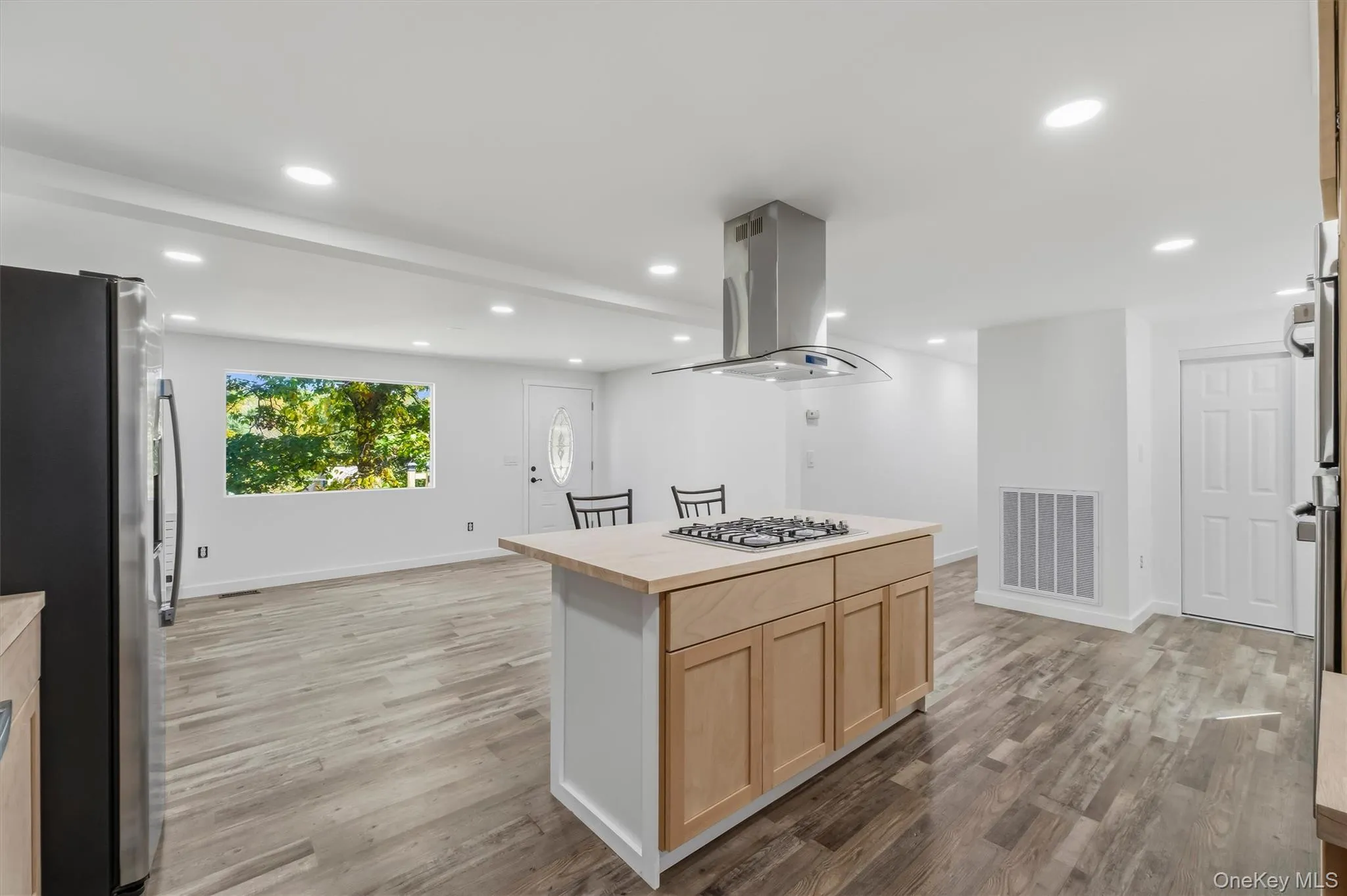 Kitchen island with a built-in gas cooktop, stainless steel range hood, wood-finish flooring, recessed lighting, and white walls Kitchen island with a built-in gas cooktop, stainless steel range hood, wood-finish flooring, recessed lighting, and white walls