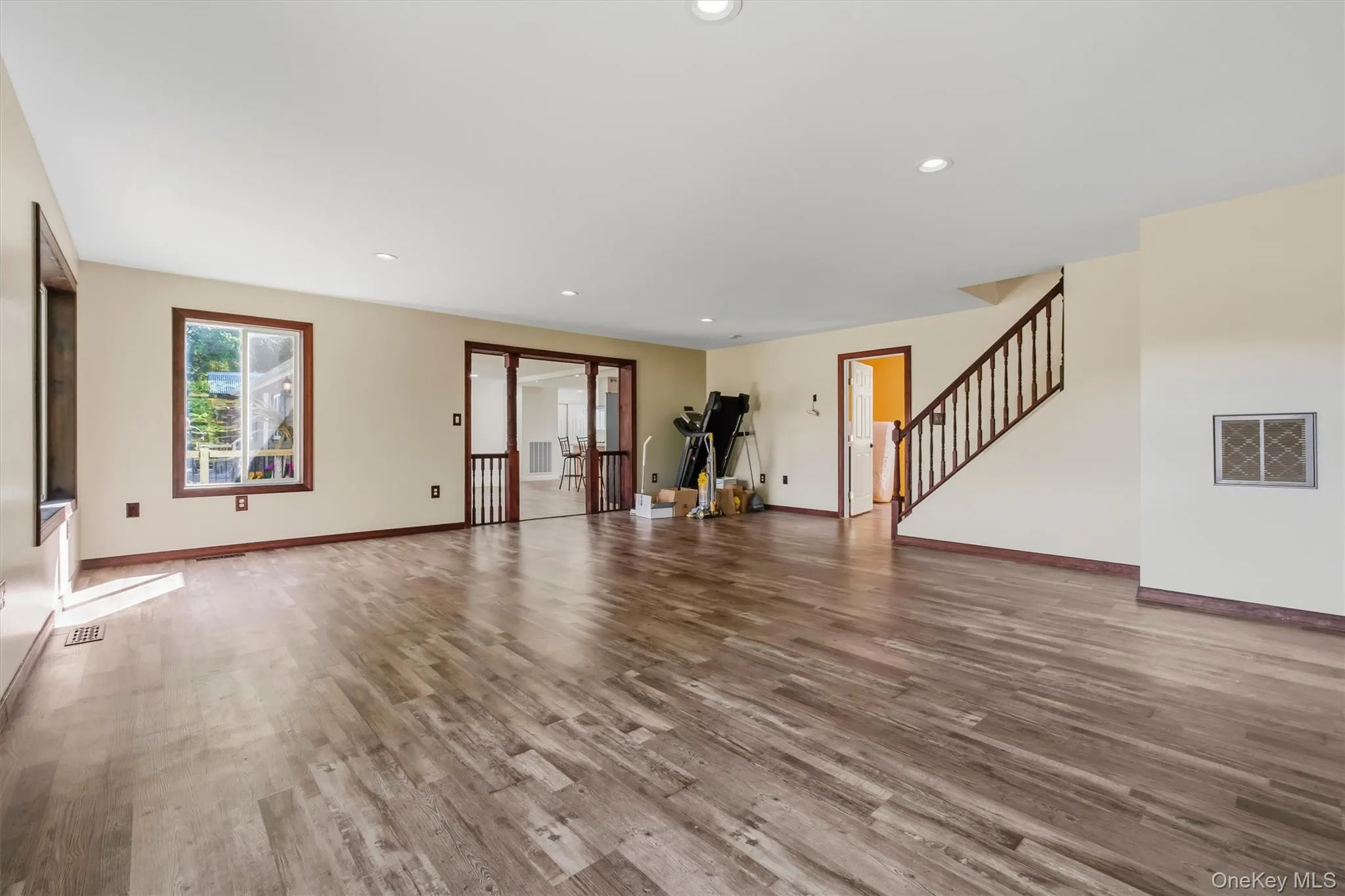 Spacious livingroom featuring wood-finish flooring, recessed lighting, and a prominent staircase with dark wood railings Spacious livingroom featuring wood-finish flooring, recessed lighting, and a prominent staircase with dark wood railings