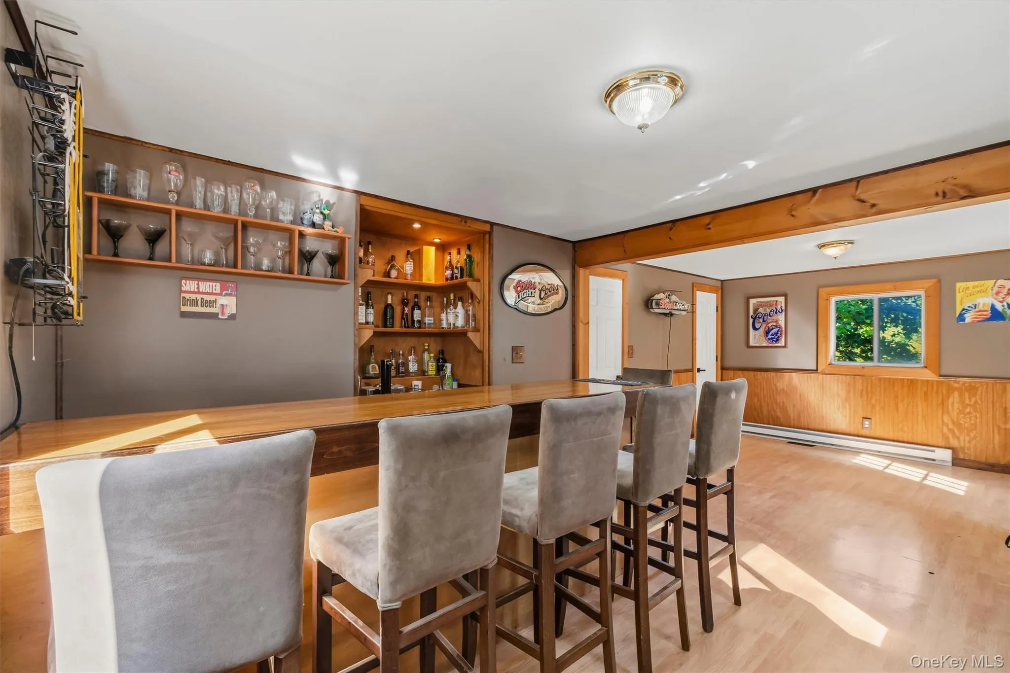 Wood-finish flooring with a built-in bar, wood paneling, and an integrated corner shelving unit Wood-finish flooring with a built-in bar, wood paneling, and an integrated corner shelving unit