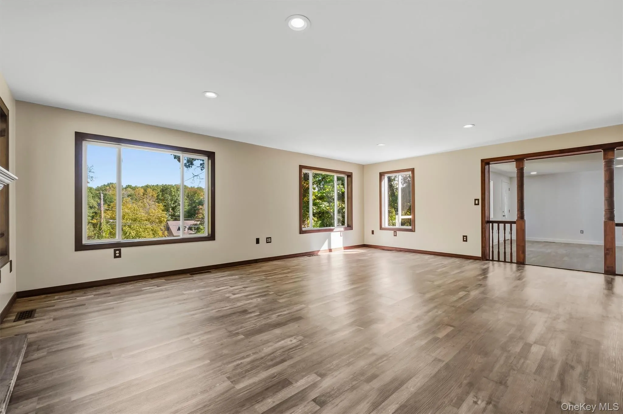 Recessed lighting, wood-finish flooring, multiple windows with dark wood trim, and a built-in fireplace mantle Recessed lighting, wood-finish flooring, multiple windows with dark wood trim, and a built-in fireplace mantle