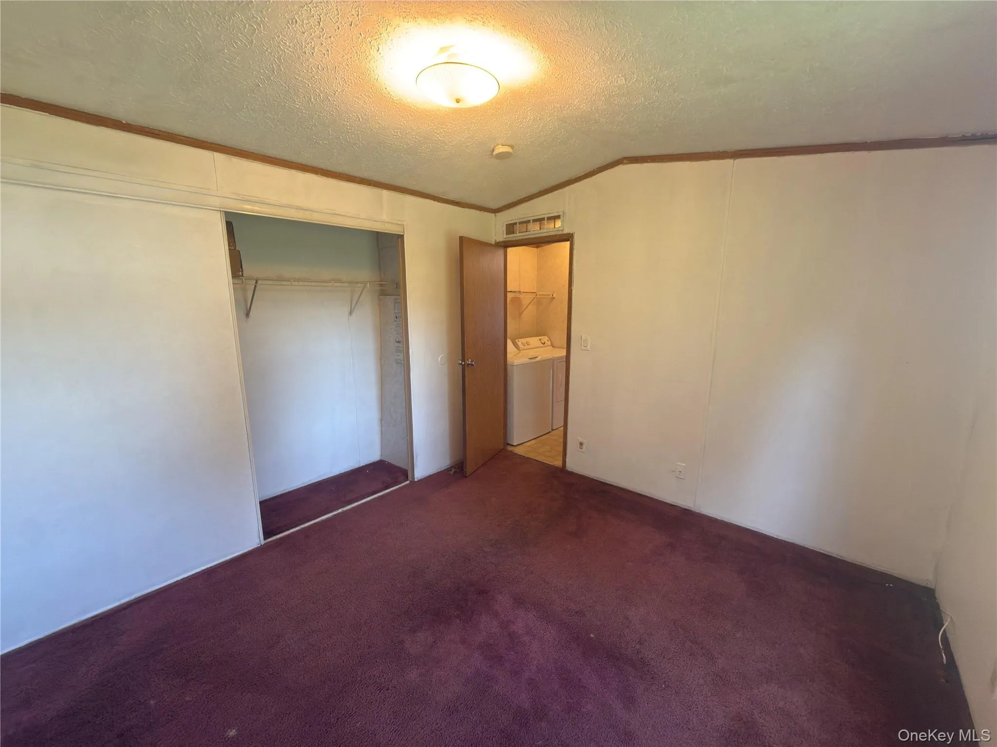 Room with carpet flooring, overhead flush mount lighting, and a closet featuring a sliding door and interior shelving Room with carpet flooring, overhead flush mount lighting, and a closet featuring a sliding door and interior shelving