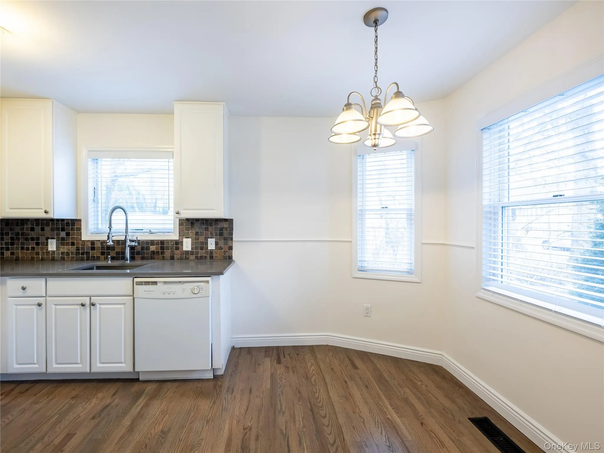 Kitchen featuring white cabinetry, dark countertop, tile backsplash, stainless steel faucet, and wood flooring Kitchen featuring white cabinetry, dark countertop, tile backsplash, stainless steel faucet, and wood flooring