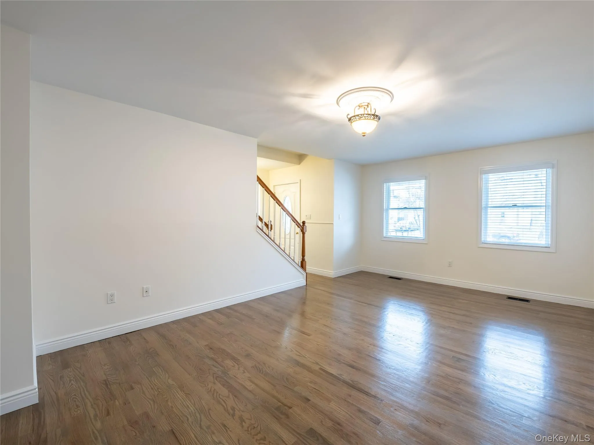 Spacious living room featuring hardwood flooring, two large windows, and a decorative ceiling-mounted light fixture Spacious living room featuring hardwood flooring, two large windows, and a decorative ceiling-mounted light fixture