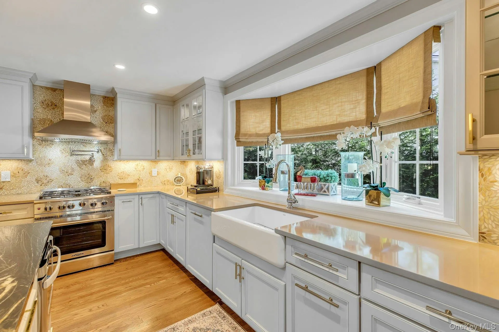 White cabinetry, light countertops, wood-finish flooring, stainless steel range with hood, and a farmhouse sink White cabinetry, light countertops, wood-finish flooring, stainless steel range with hood, and a farmhouse sink