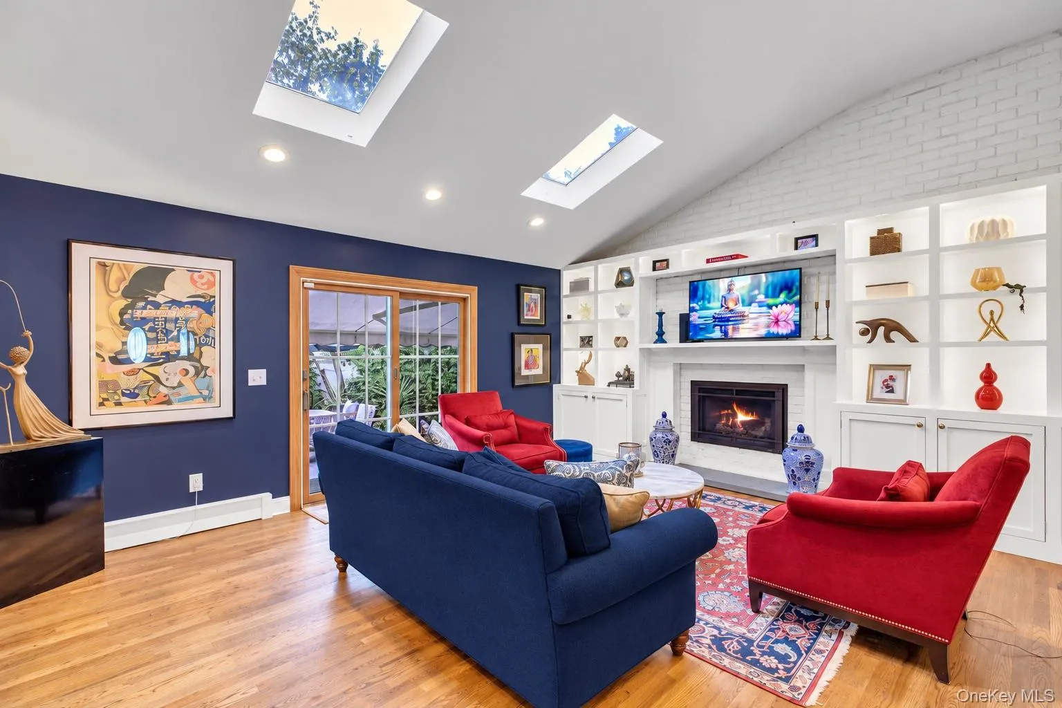 Vaulted ceiling with skylights, wood-finish flooring, built-in shelving, and a gas fireplace Vaulted ceiling with skylights, wood-finish flooring, built-in shelving, and a gas fireplace