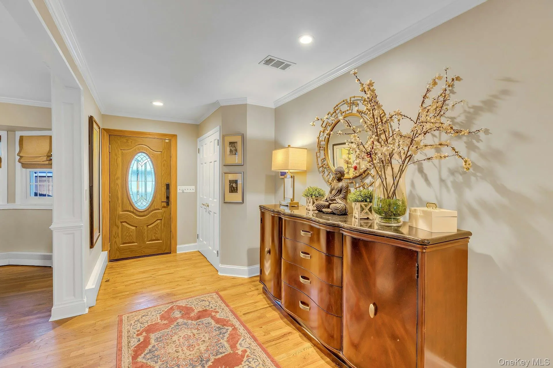 Hardwood flooring, wood entry door with oval leaded glass, white crown molding, recessed lighting, and wall-mounted picture frames Hardwood flooring, wood entry door with oval leaded glass, white crown molding, recessed lighting, and wall-mounted picture frames