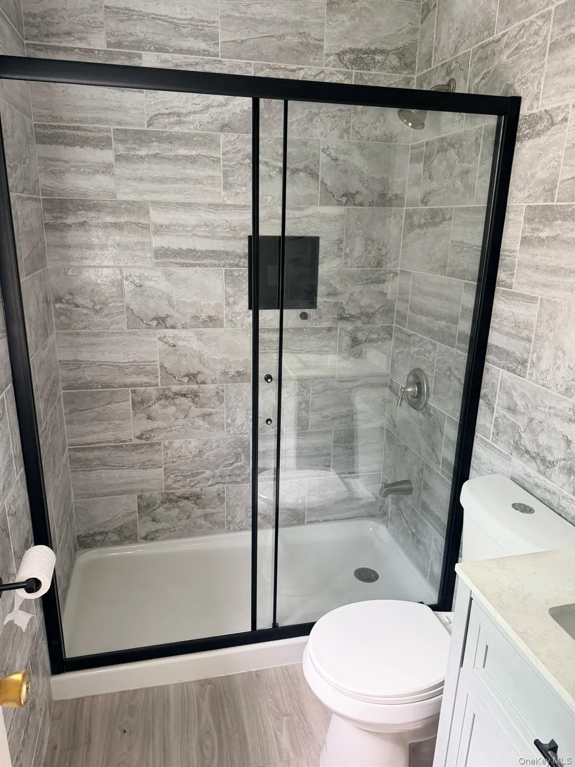 Shower enclosure featuring black-framed sliding glass doors, a built-in shower niche, and light gray tiled walls Shower enclosure featuring black-framed sliding glass doors, a built-in shower niche, and light gray tiled walls