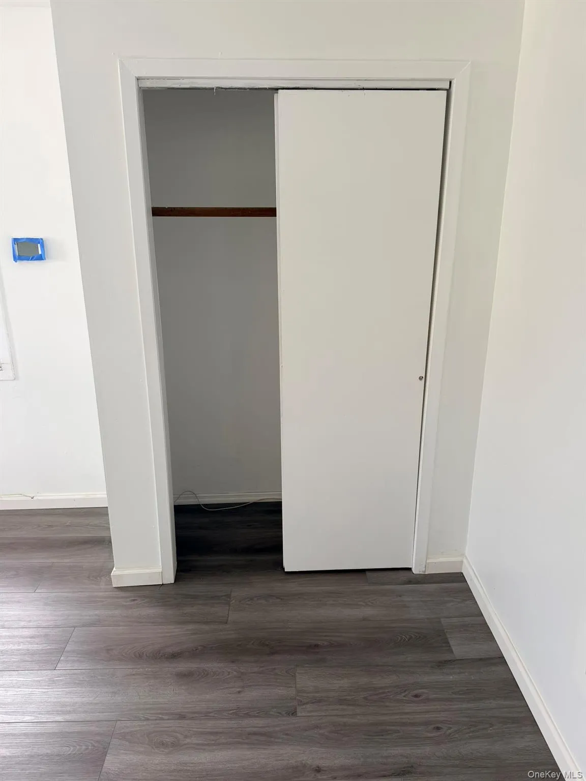 Sliding closet doors, wood-finish flooring, white walls, and a built-in closet rod Sliding closet doors, wood-finish flooring, white walls, and a built-in closet rod