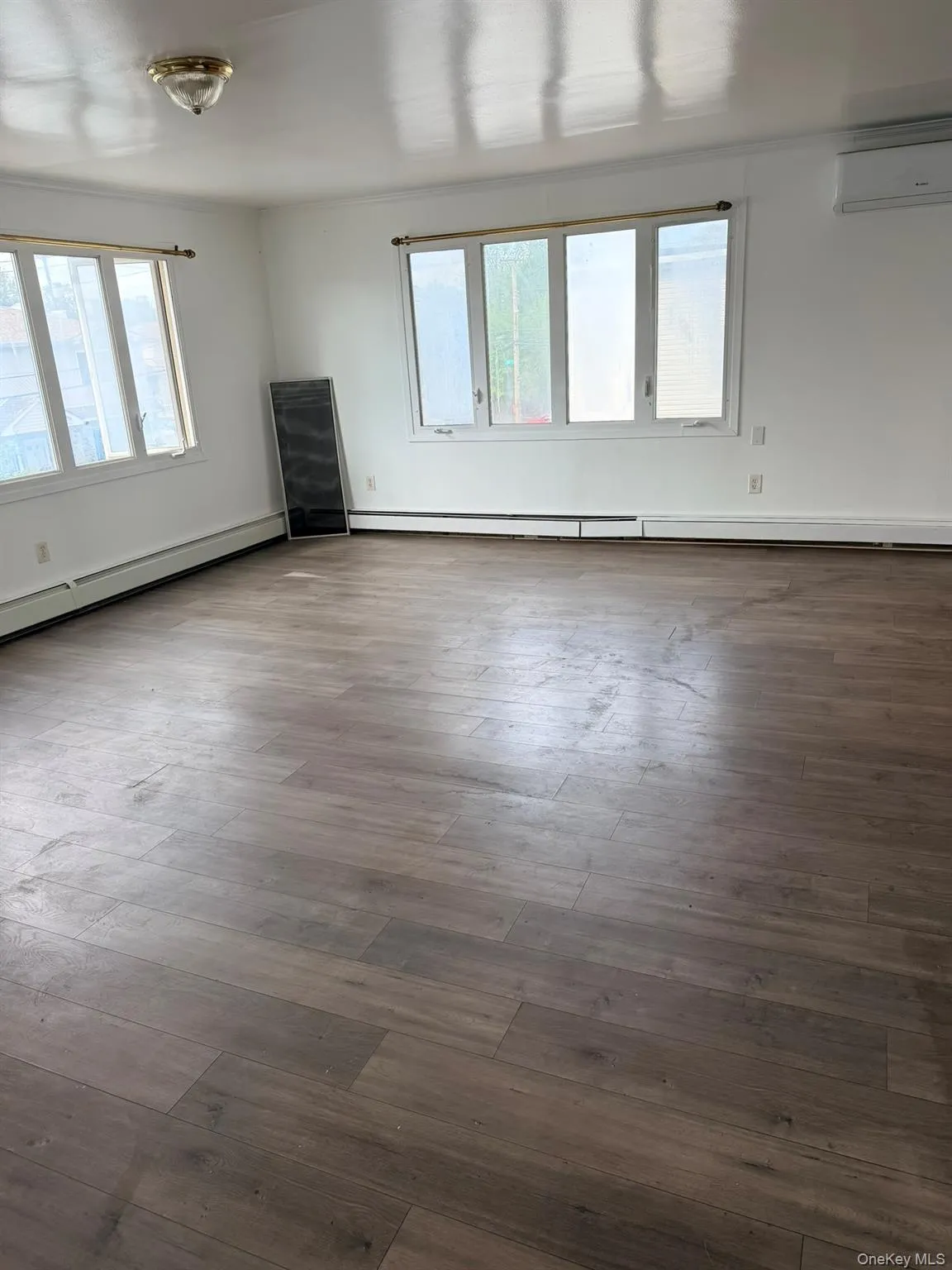 Wood-finish flooring throughout, multiple windows, and a wall-mounted air conditioning unit Wood-finish flooring throughout, multiple windows, and a wall-mounted air conditioning unit