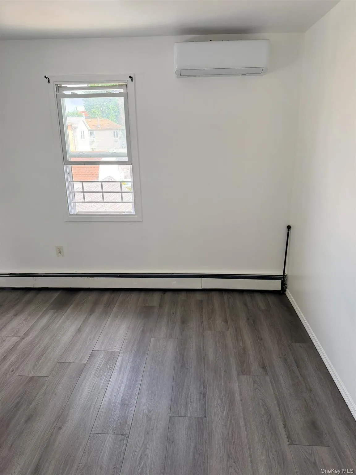 Bright, light-filled bedroom featuring wood-finish plank flooring, large operable window with natural light, split-system air conditioning unit, and clean white walls with subtle architectural trim detail Bright, light-filled bedroom featuring wood-finish plank flooring, large operable window with natural light, split-system air conditioning unit, and clean white walls with subtle architectural trim detail