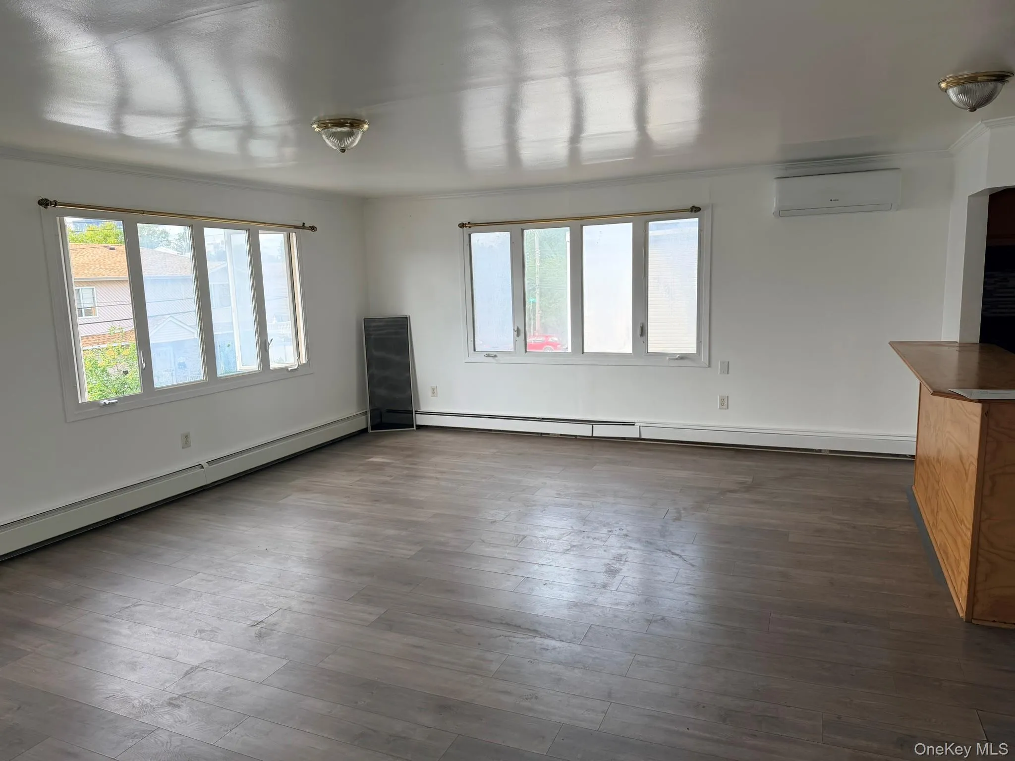 Expansive room with wood-finish flooring, multiple windows, built-in air conditioning unit, and a built-in counter with wood-finish cabinetry Expansive room with wood-finish flooring, multiple windows, built-in air conditioning unit, and a built-in counter with wood-finish cabinetry