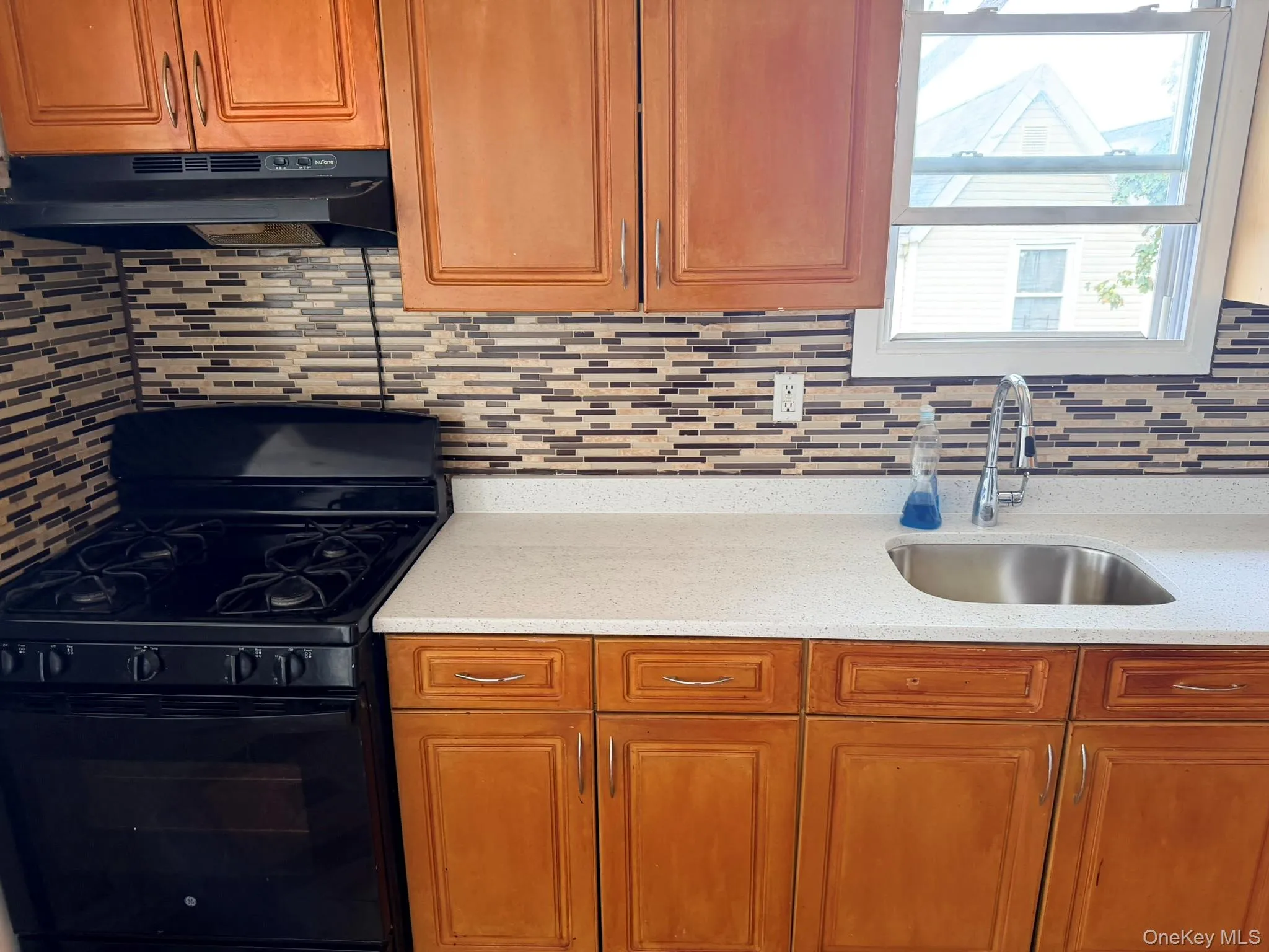 Wood-finish cabinetry paired with a black gas range and stainless-steel sink Wood-finish cabinetry paired with a black gas range and stainless-steel sink