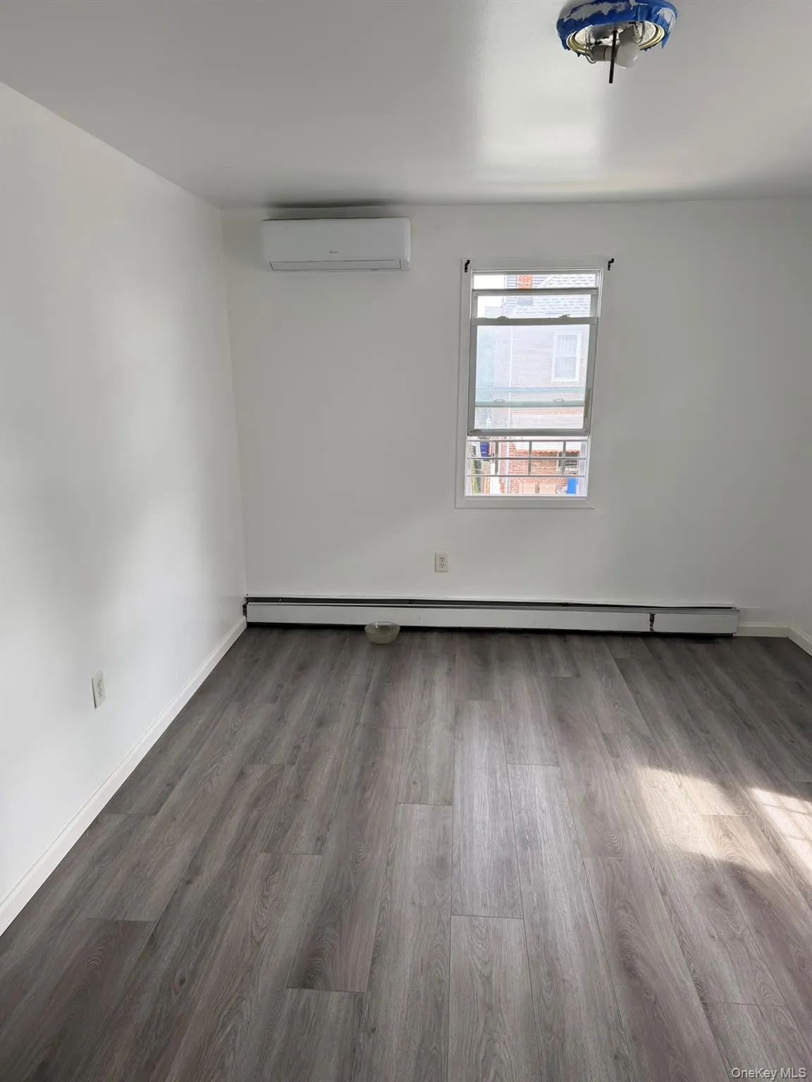 Wood-finish flooring with white walls, a single window, and a wall-mounted mini-split AC unit Wood-finish flooring with white walls, a single window, and a wall-mounted mini-split AC unit