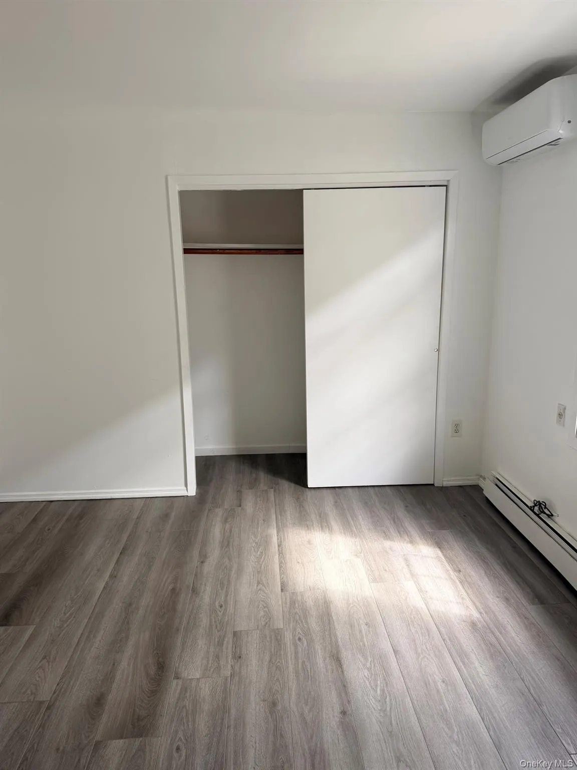 Wood-finish flooring, white walls, built-in closet with sliding doors, and a wall-mounted mini-split unit Wood-finish flooring, white walls, built-in closet with sliding doors, and a wall-mounted mini-split unit