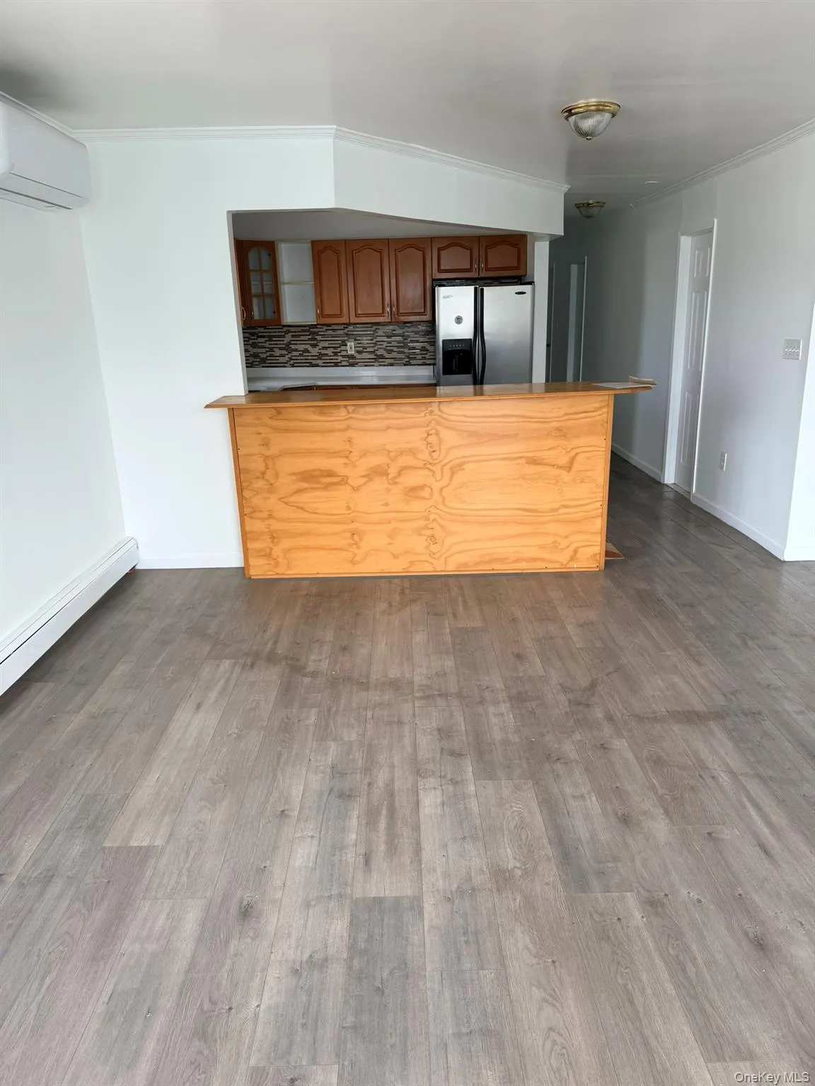 Wood-finish flooring, built-in breakfast bar, kitchen with stainless steel refrigerator, wood cabinetry, and mosaic tile backsplash Wood-finish flooring, built-in breakfast bar, kitchen with stainless steel refrigerator, wood cabinetry, and mosaic tile backsplash