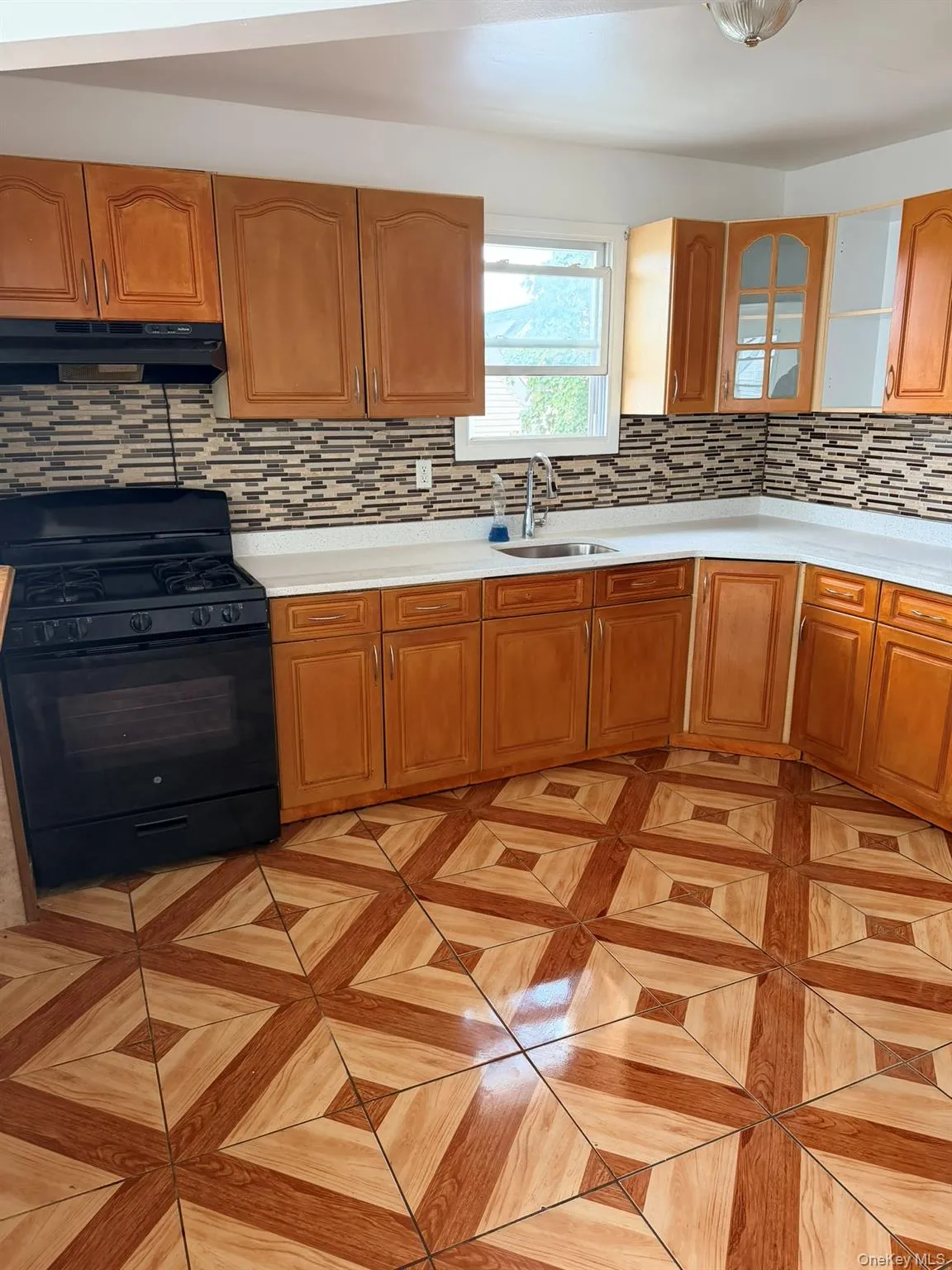 Kitchen featuring wood-finish cabinetry, solid surface countertops, a mosaic tile backsplash, and a built-in range with an overhead vent Kitchen featuring wood-finish cabinetry, solid surface countertops, a mosaic tile backsplash, and a built-in range with an overhead vent