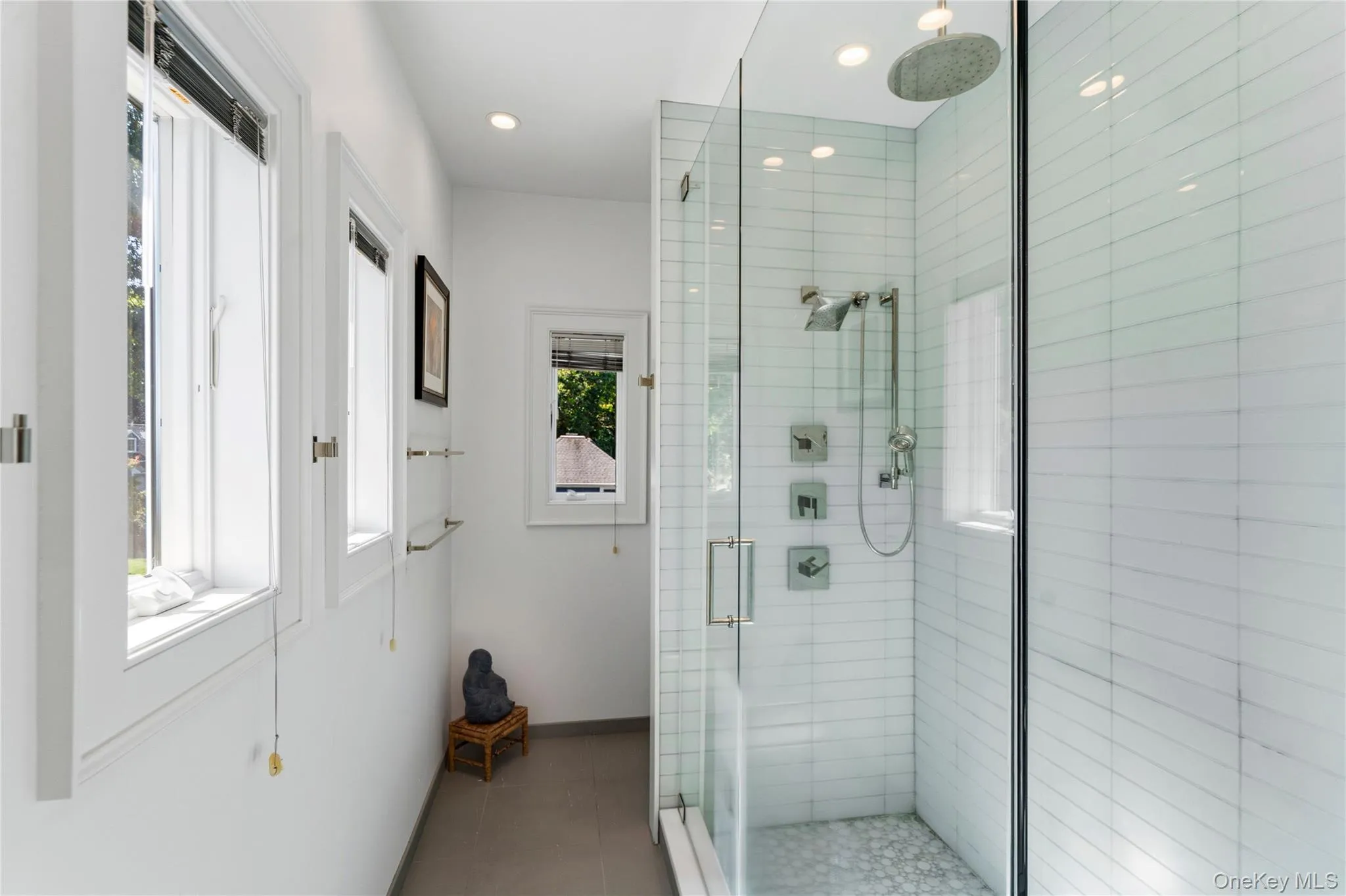 Walk-in shower featuring glass paneling, white subway tile surround, rainfall showerhead, handheld shower sprayer, and stone tile flooring Walk-in shower featuring glass paneling, white subway tile surround, rainfall showerhead, handheld shower sprayer, and stone tile flooring