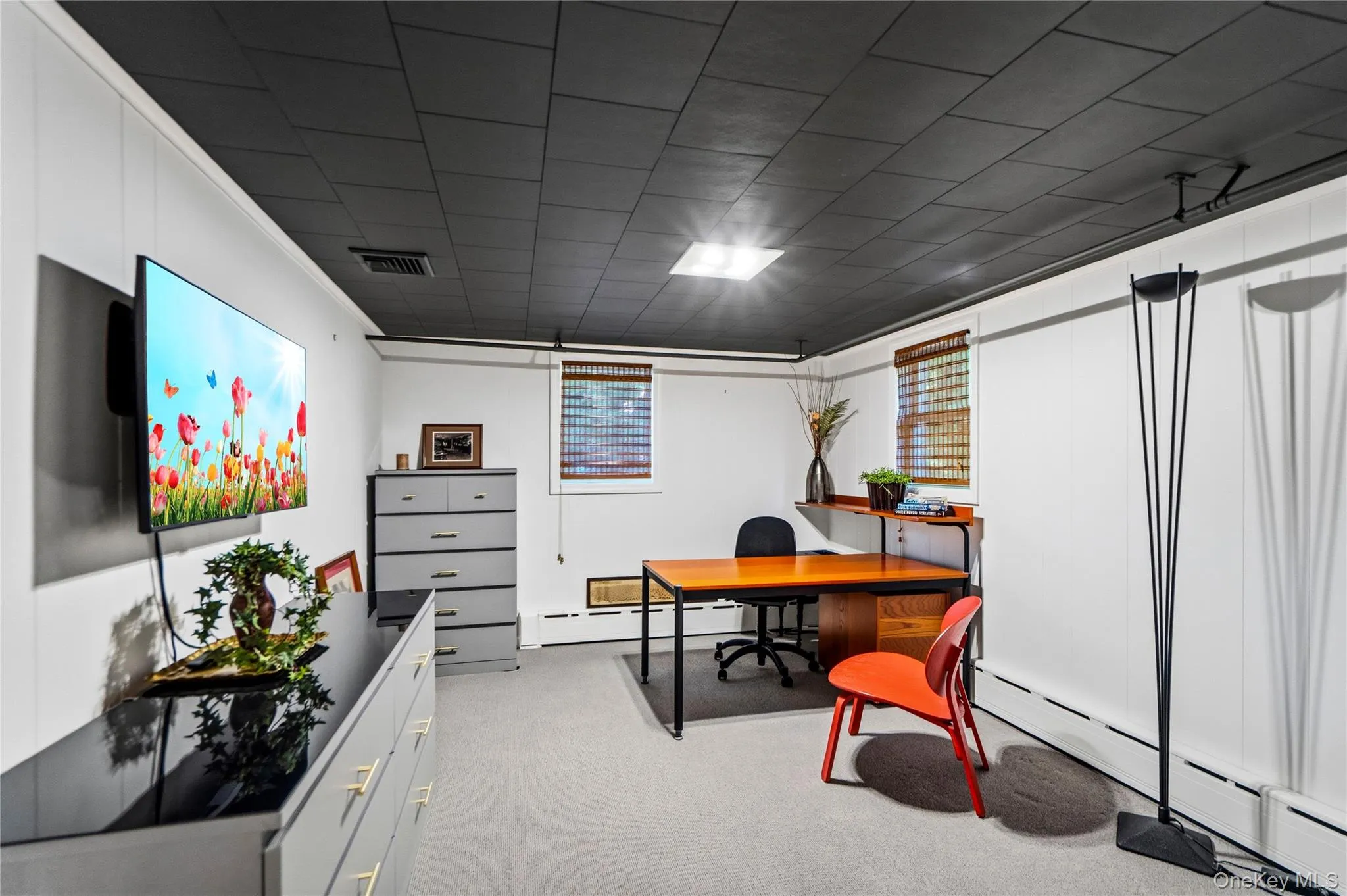 Interior space featuring charcoal-toned ceiling tiles, white wall paneling, neutral carpeting, and built-in shelving Interior space featuring charcoal-toned ceiling tiles, white wall paneling, neutral carpeting, and built-in shelving