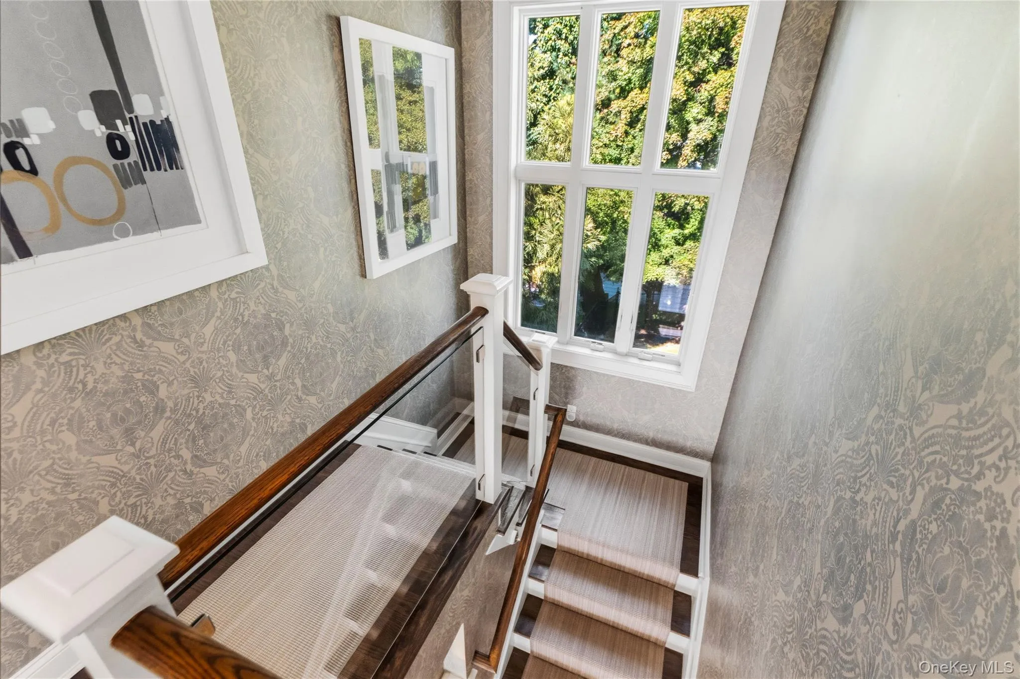 Staircase featuring glass panel railings, wood handrails, patterned wall covering, and a multi-pane window Staircase featuring glass panel railings, wood handrails, patterned wall covering, and a multi-pane window